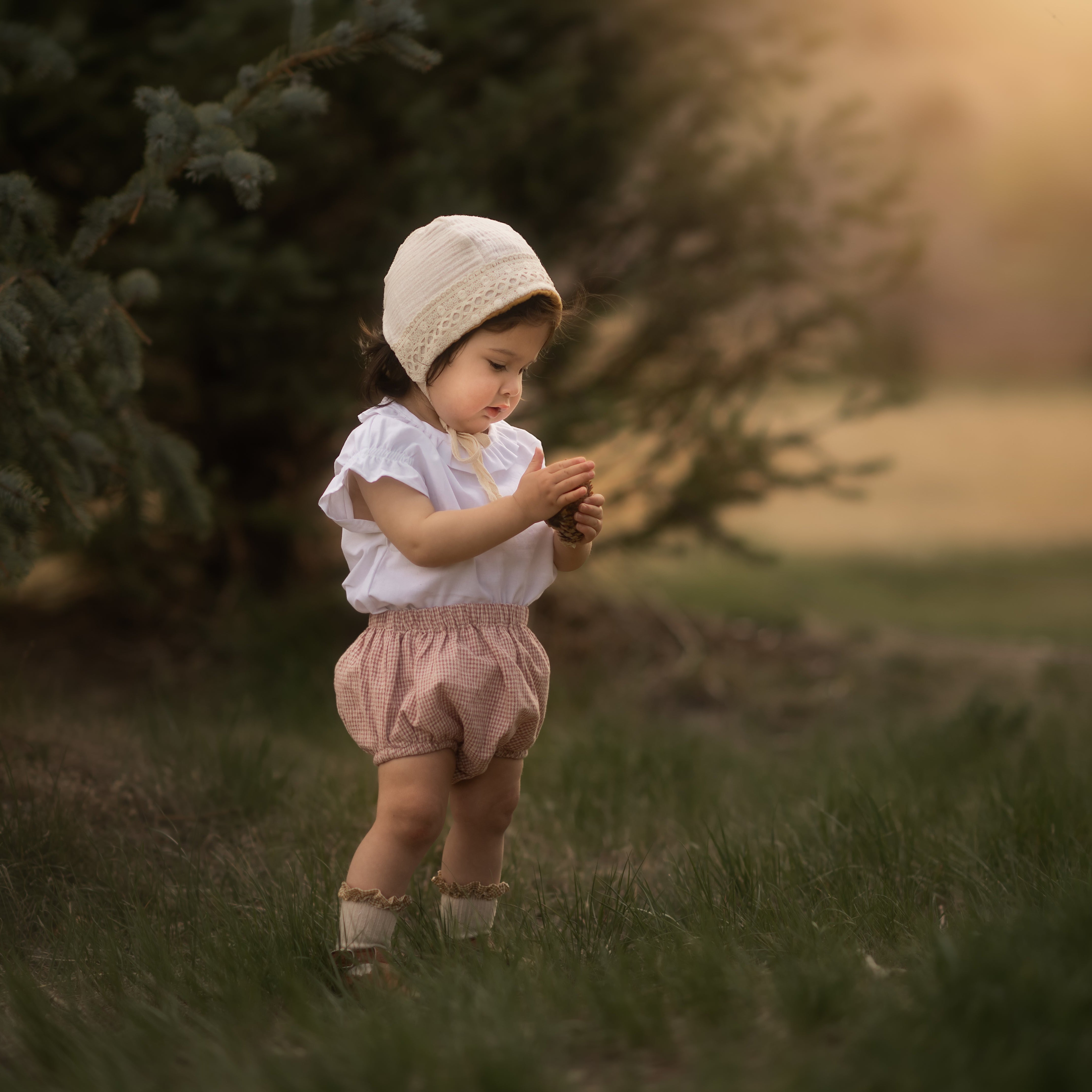 Baby in a bonnet and bloomers in a blurred field playing with her hands