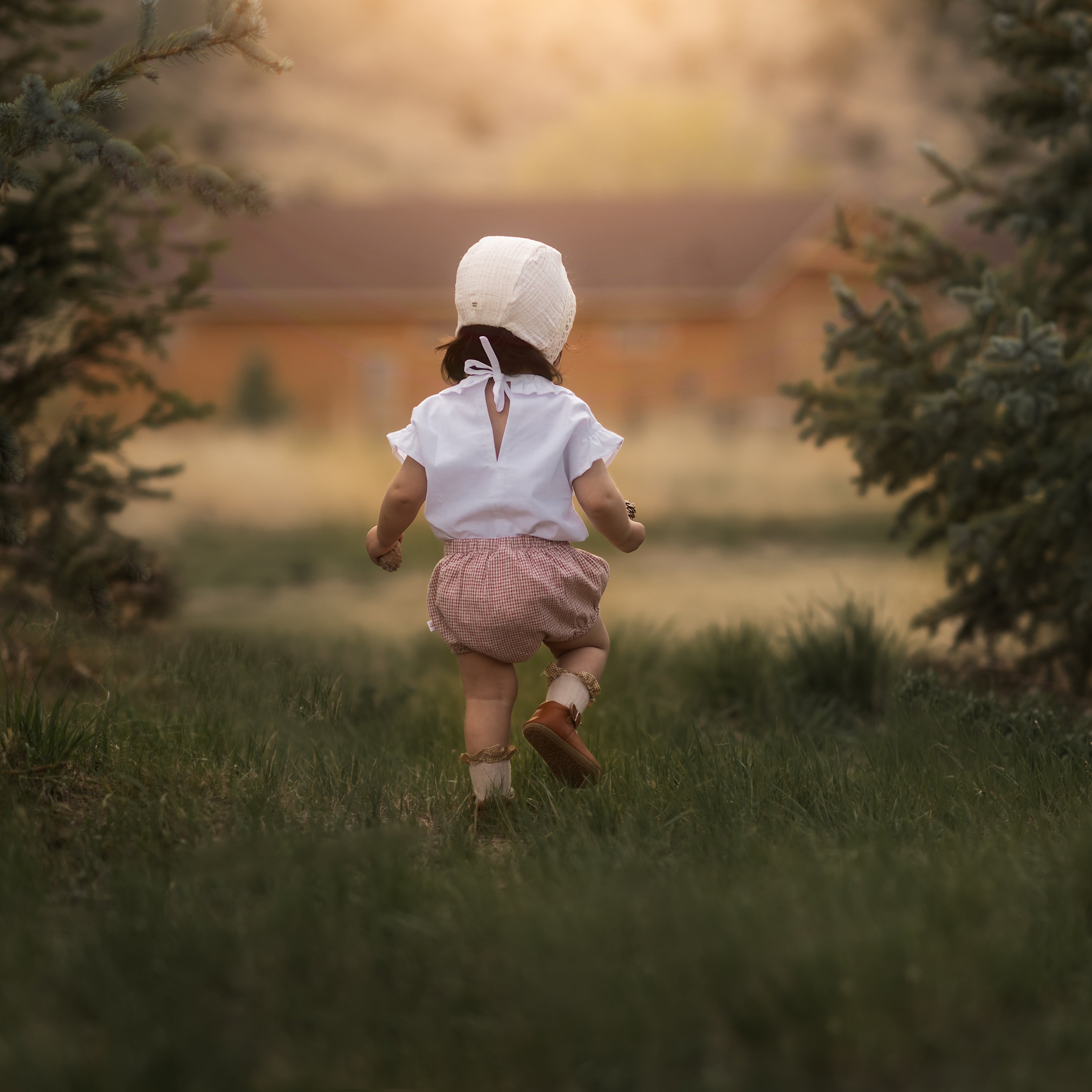 Baby in a bonnet and bloomers in a blurred field walking away