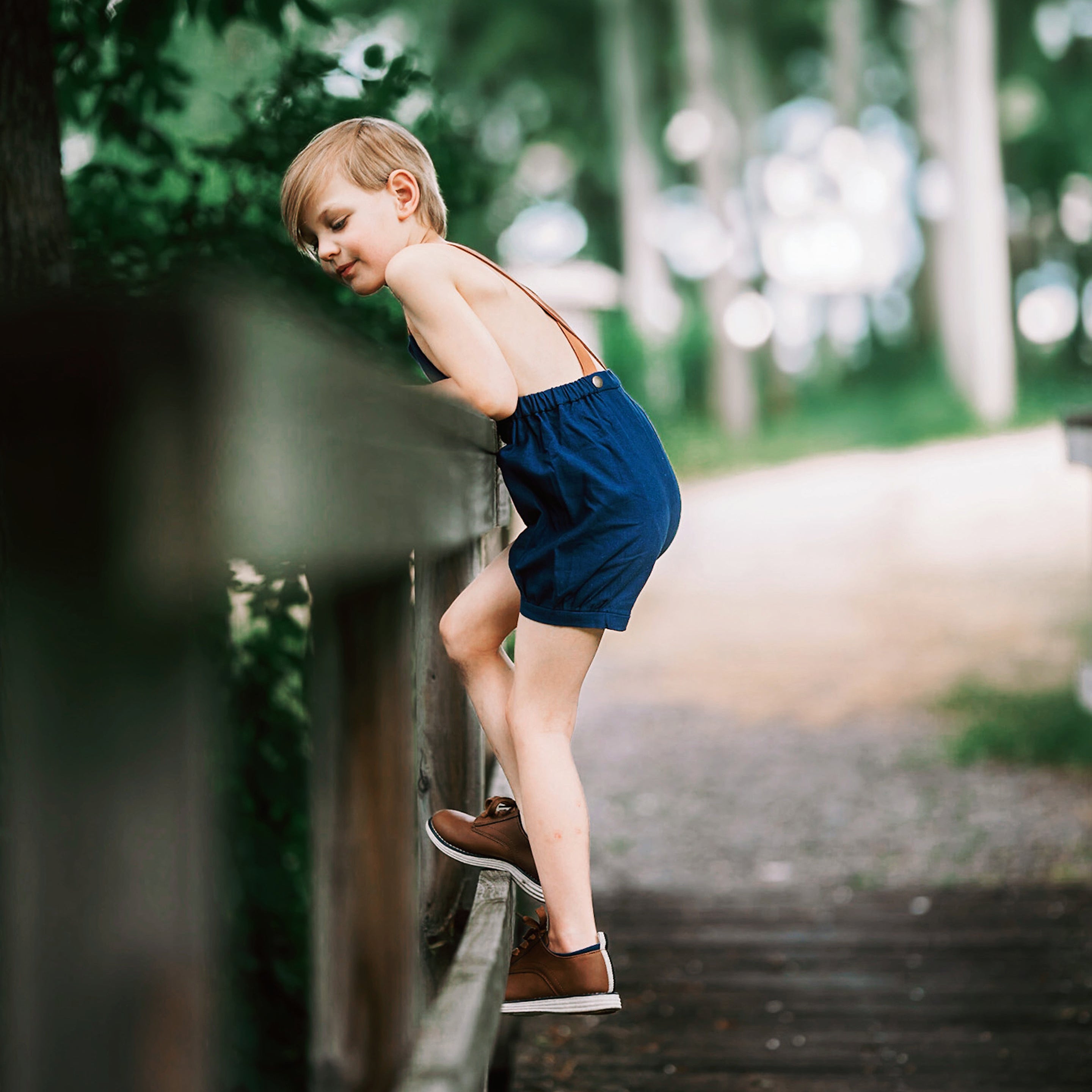 Boy in navy overalls climbing over a fence