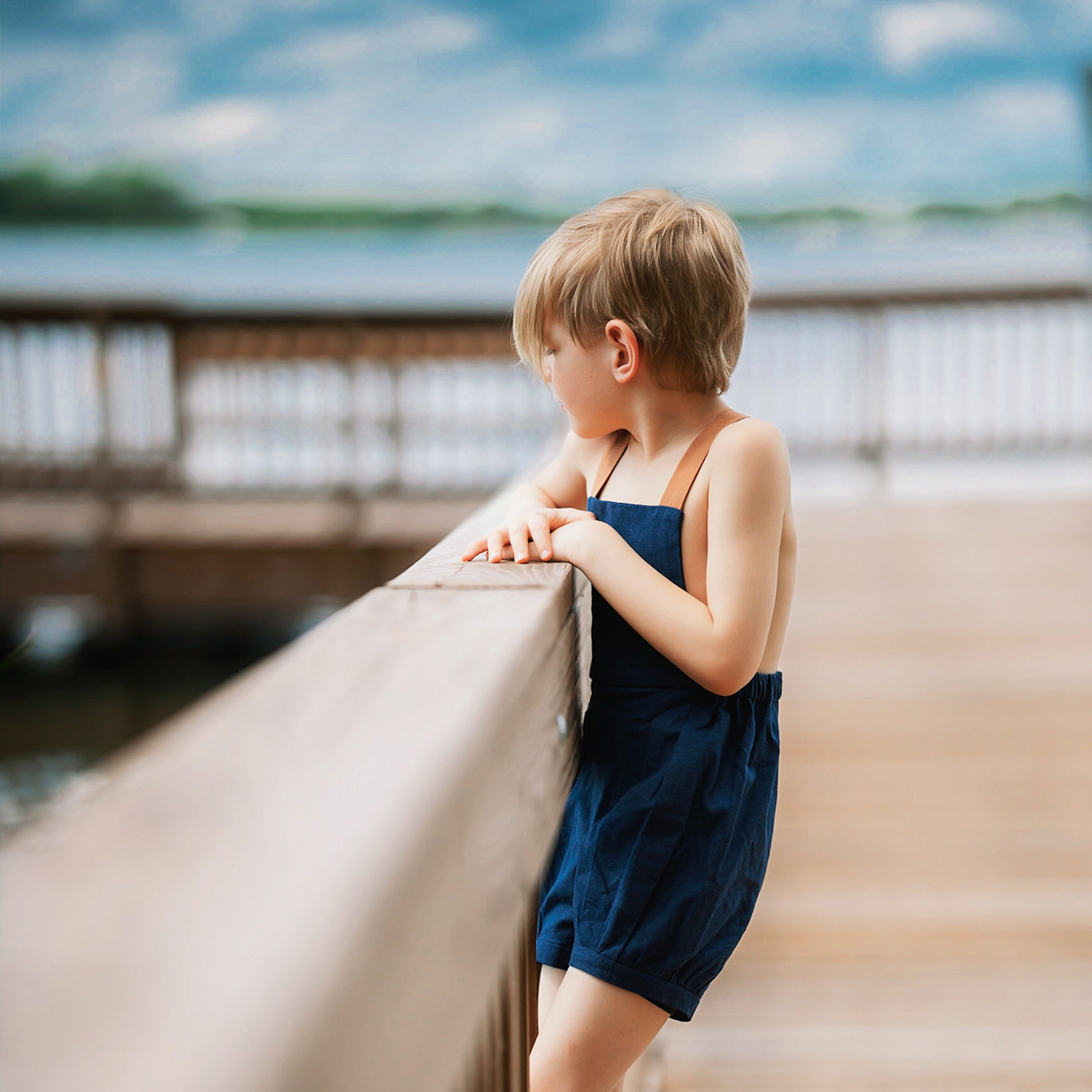 Boy in navy linen overalls by water