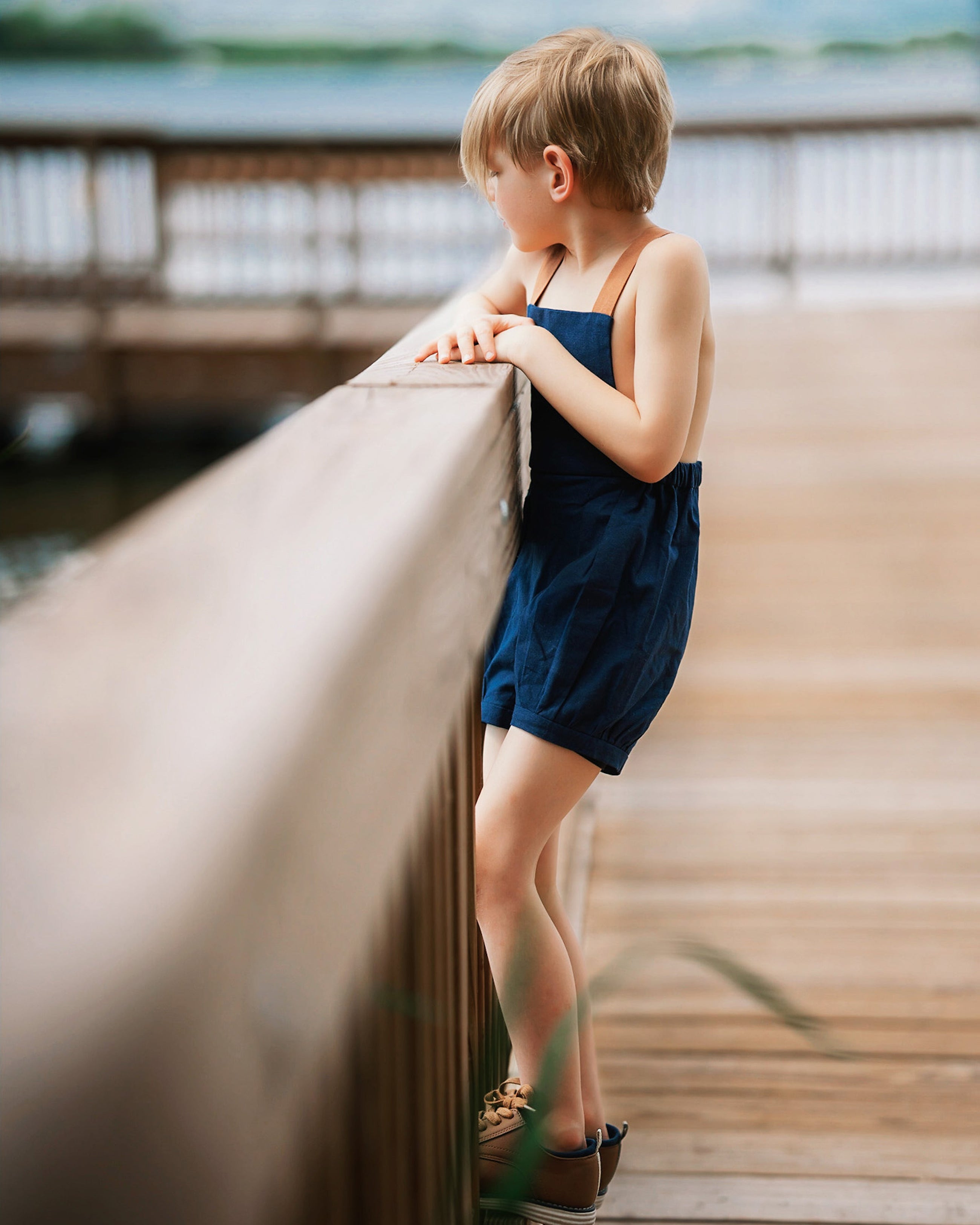 Boy in navy linen overalls by water