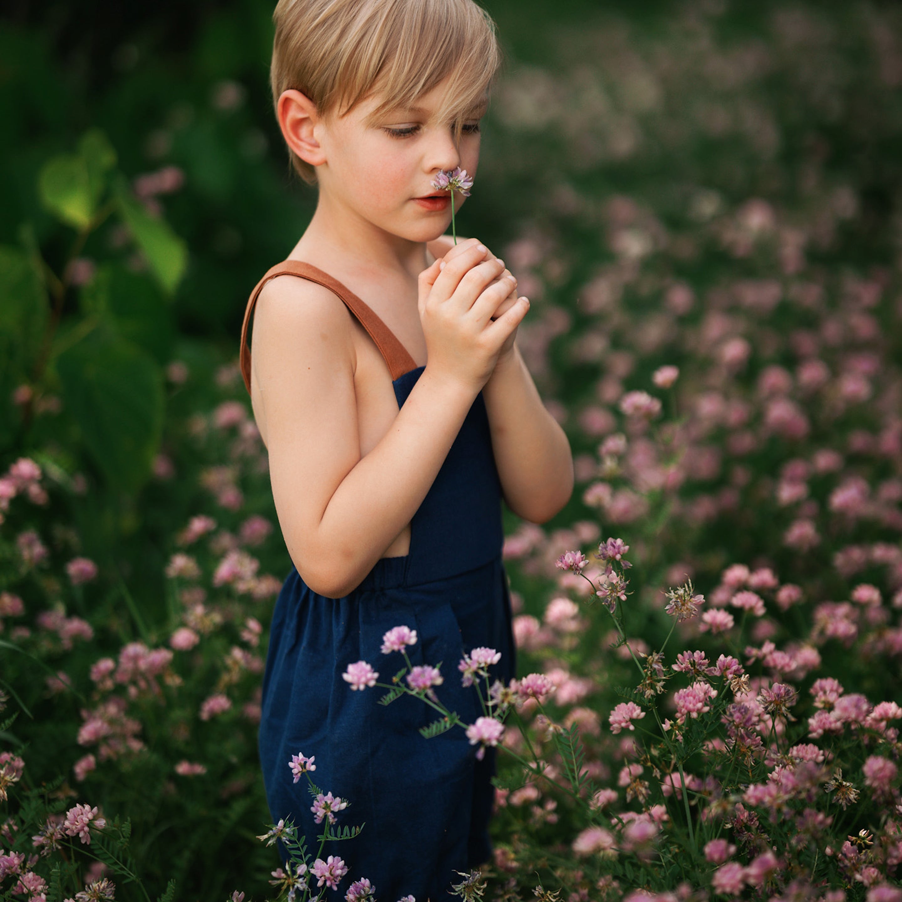 Boy in navy overalls smelling flowers in a field of flowers