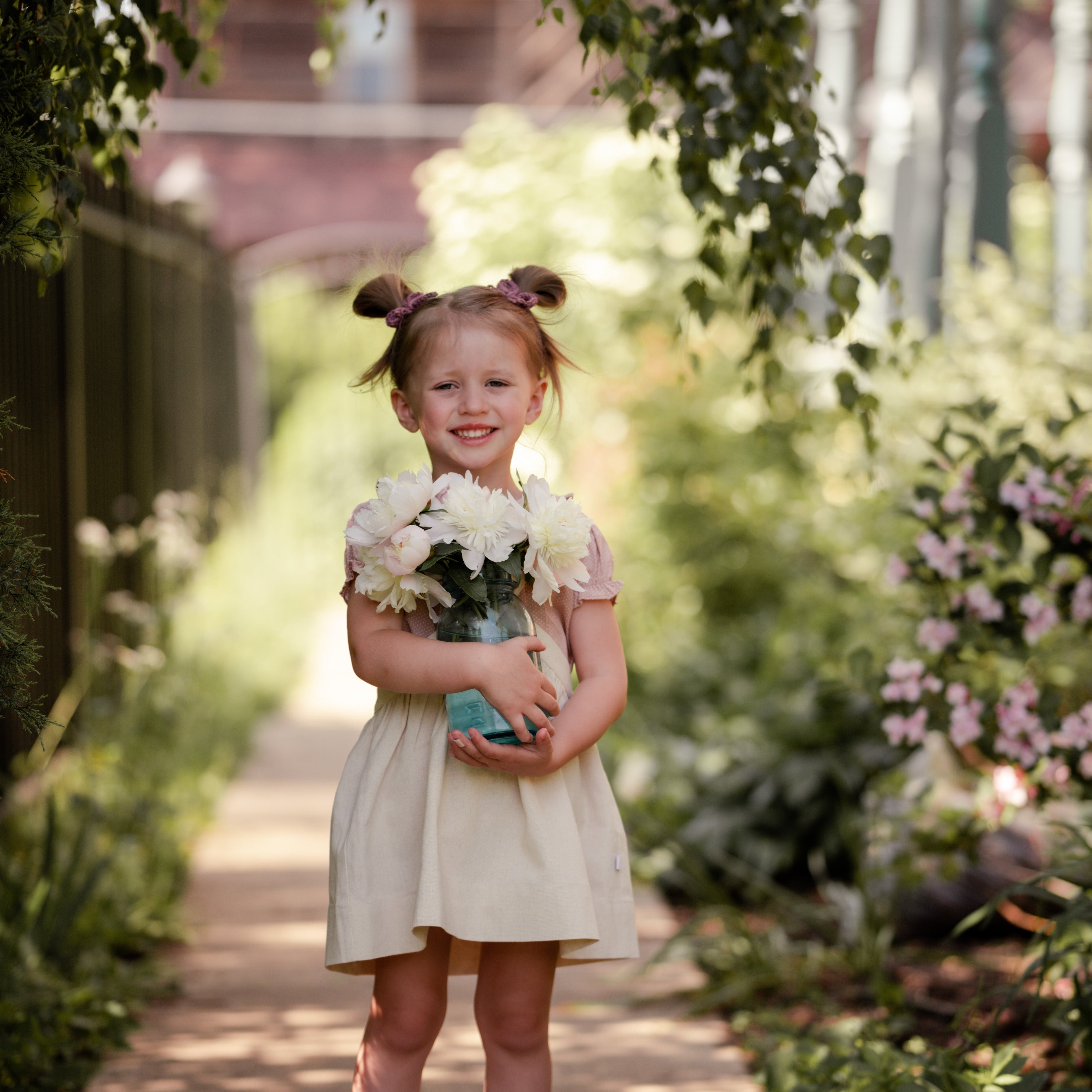 Young girl holding flowers in a garden setting wearing a natural linen pinafore