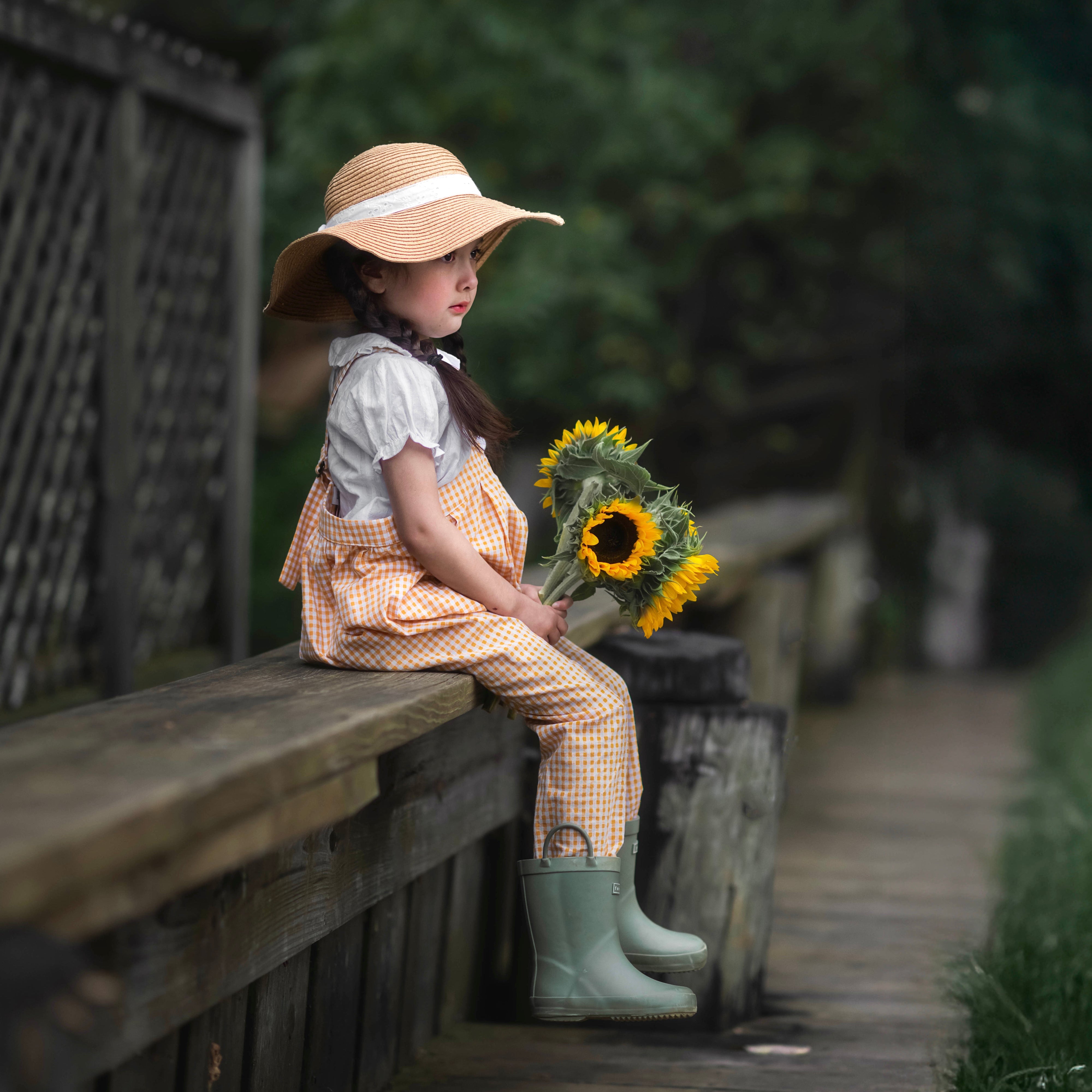 Girl sitting on a wooden bench holding sunflowers in a natural setting
