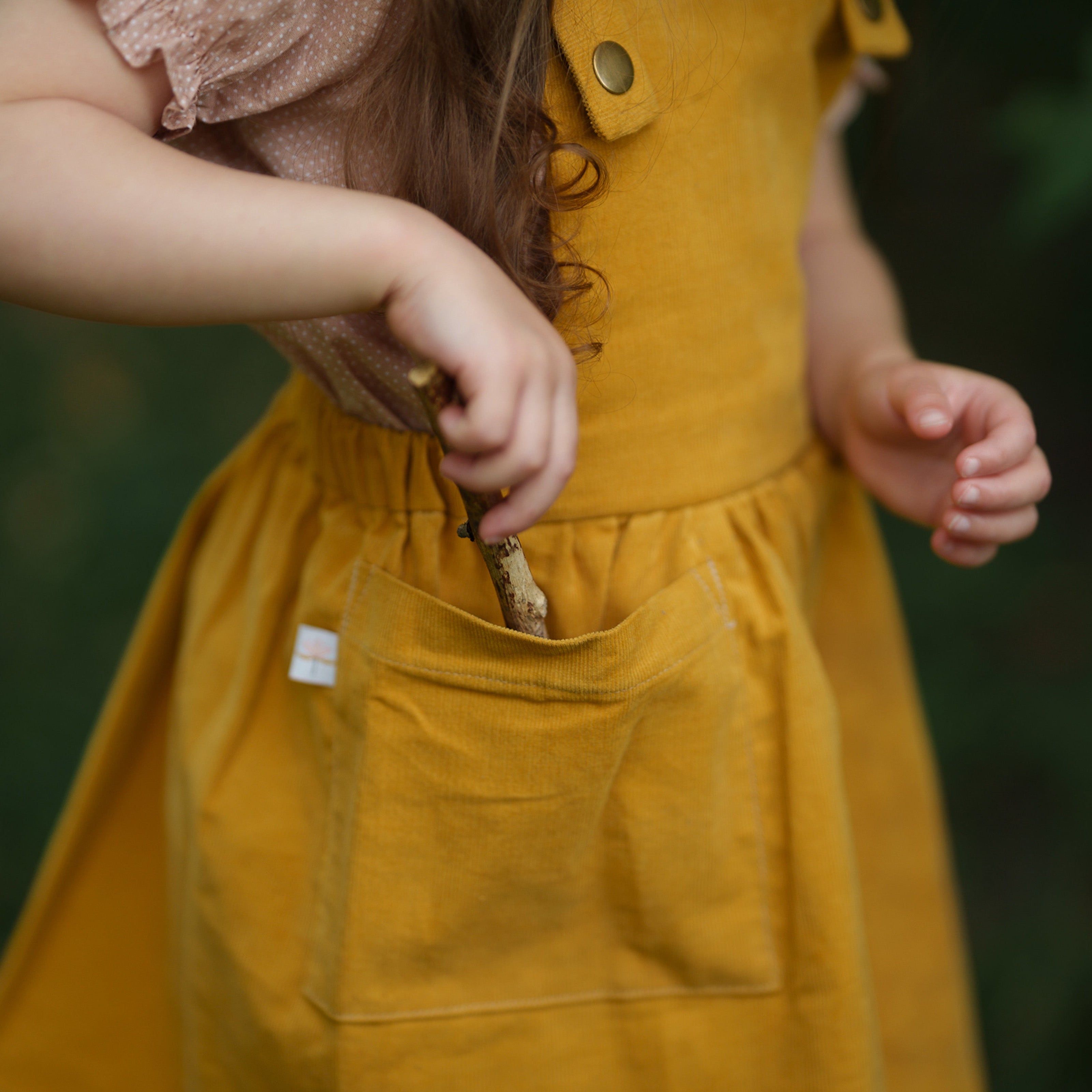 Detail view of the large patch pocket on the Mustard Pinafore worn by a model, emphasizing its practical design and the use of repurposed materials in our sustainable collection.