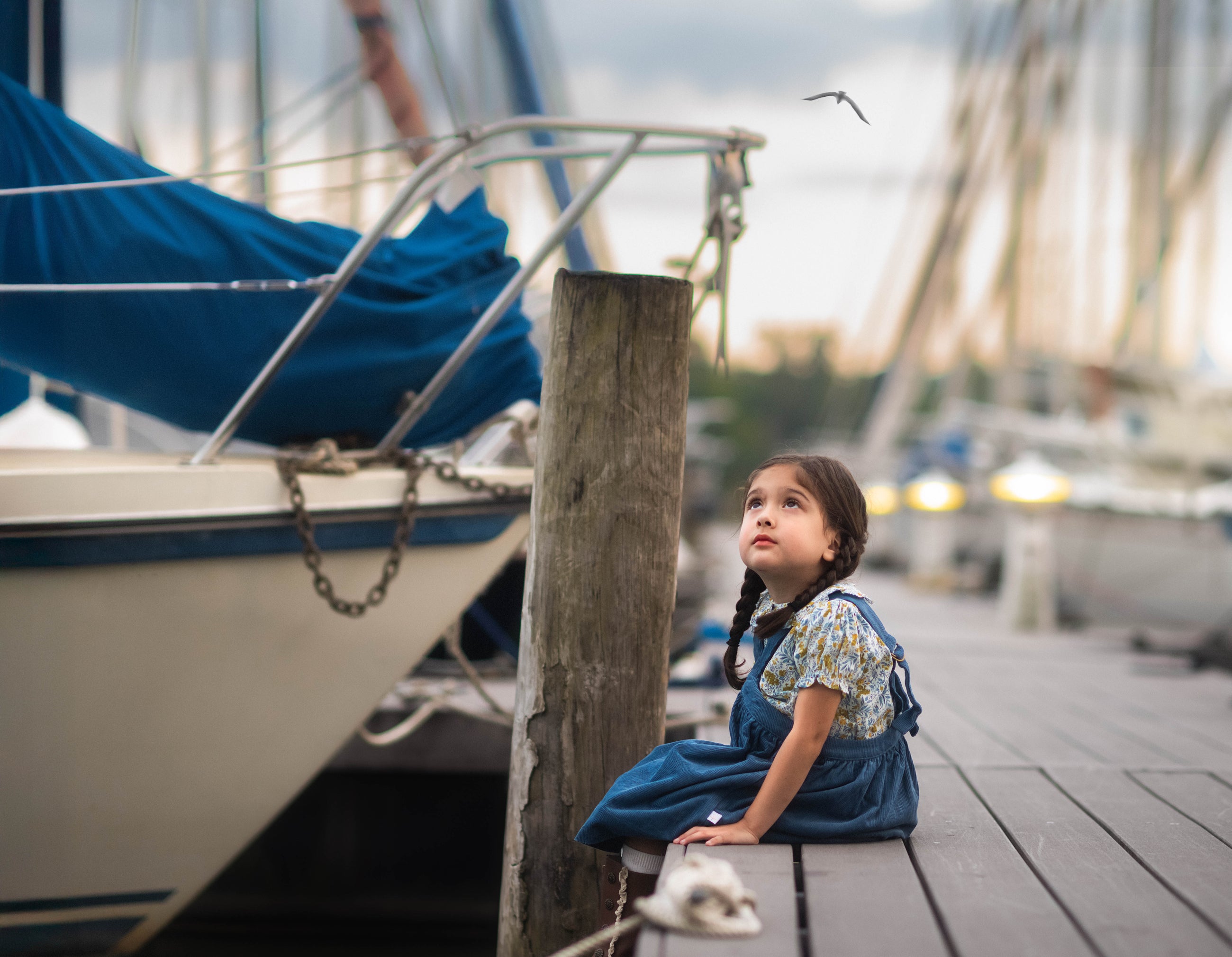 Young girl sitting on a dock by a boat, looking up at the sky.