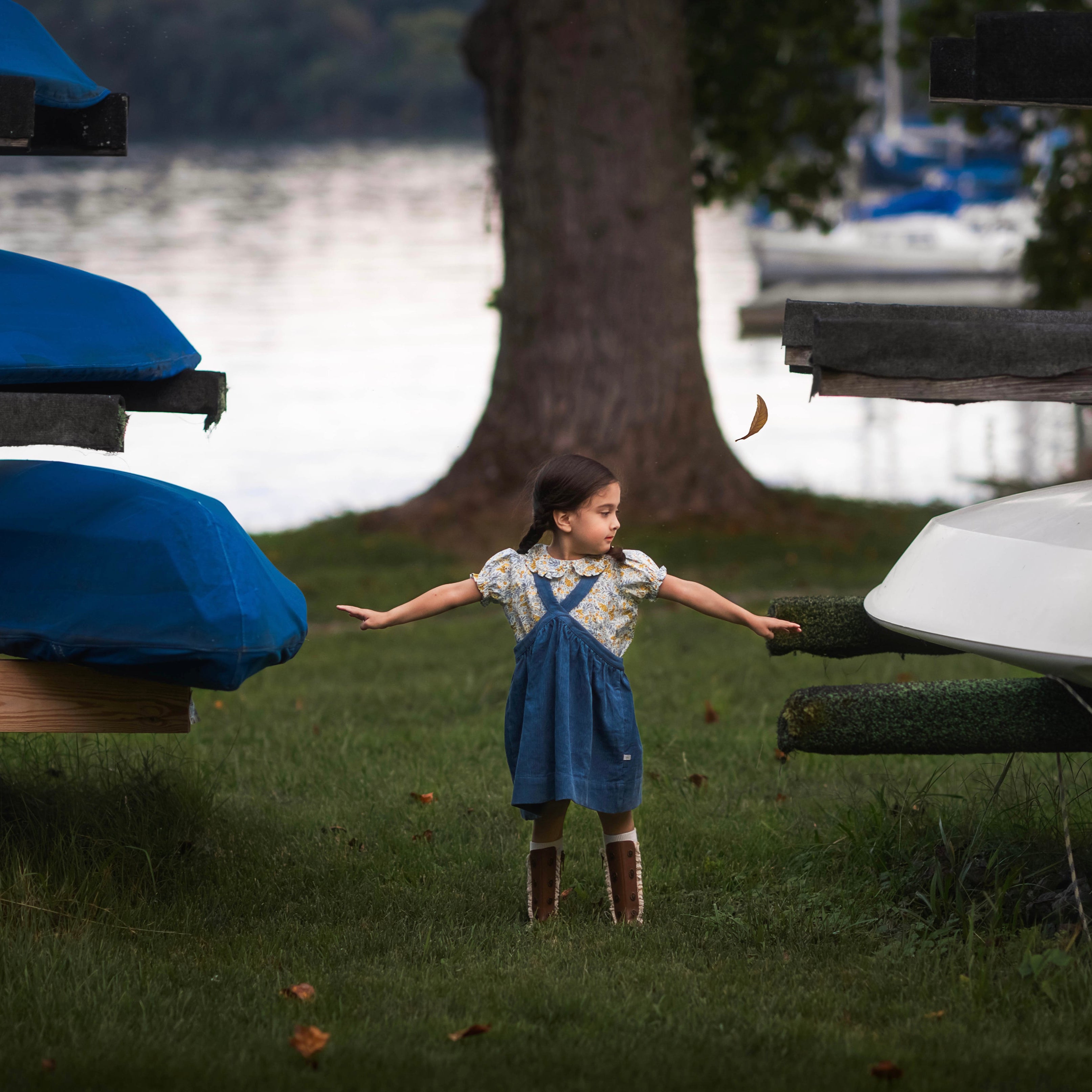 Young girl in a blue dress standing near canoes by a lake