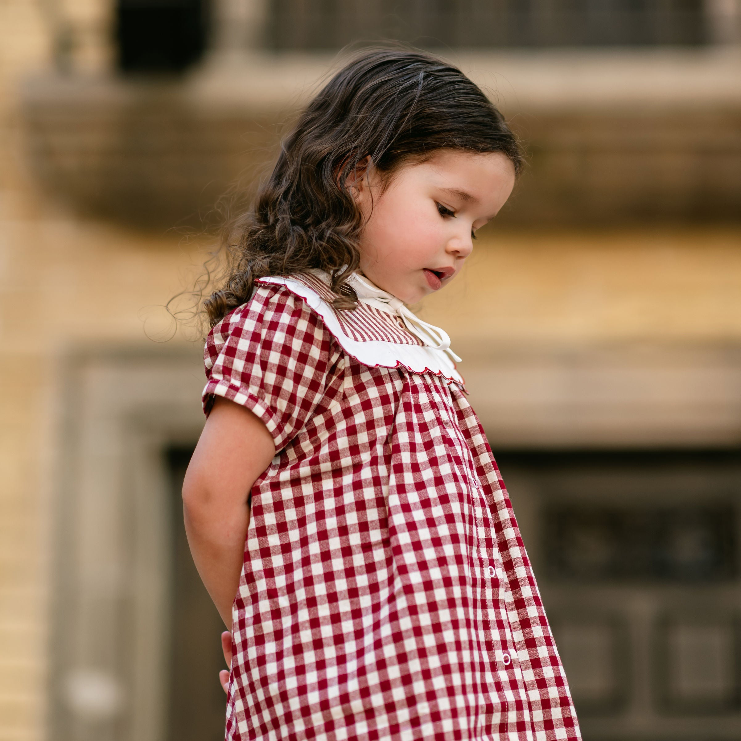 Young girl in a red and white checkered dress standing outdoors.