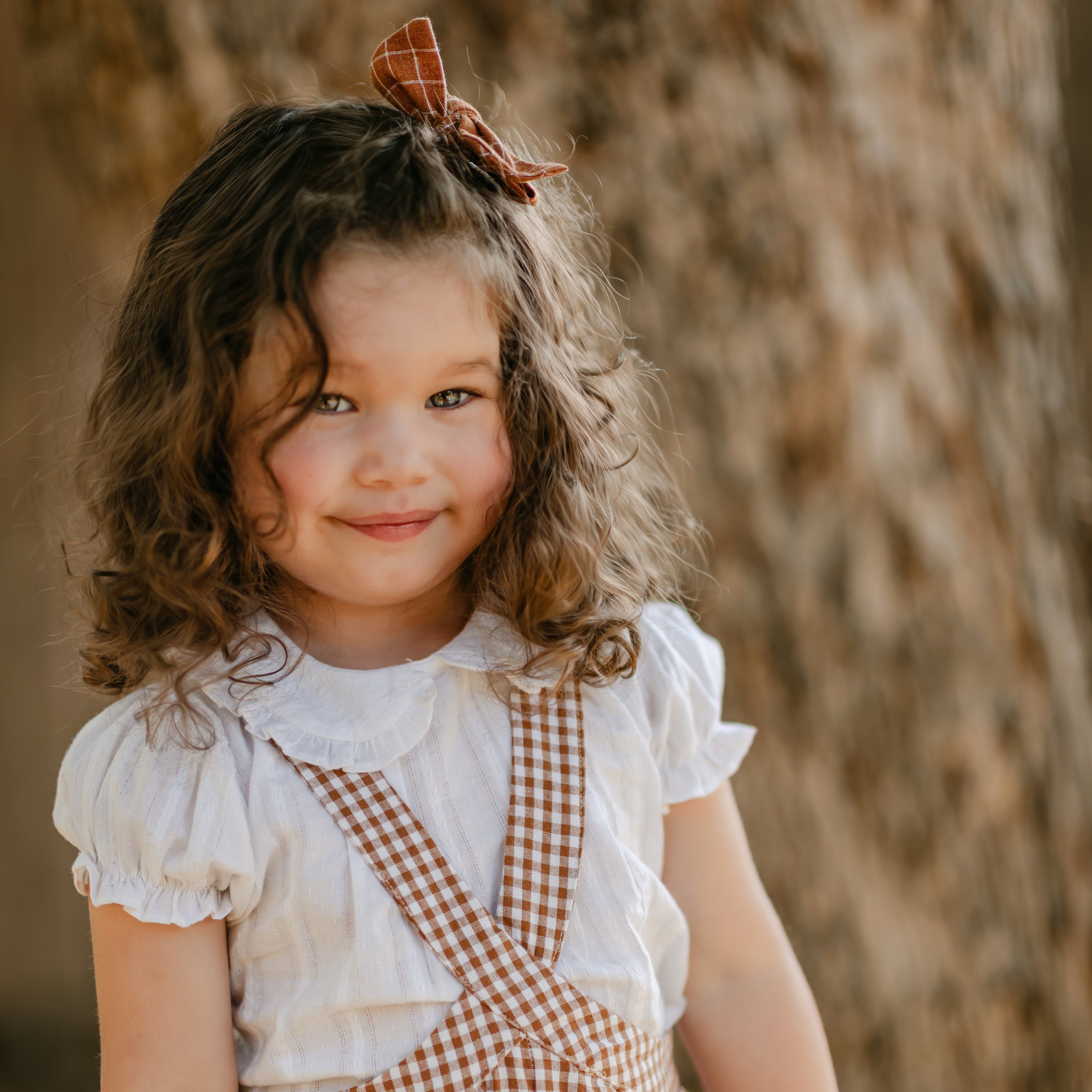 Young girl in a checkered outfit standing against a natural background