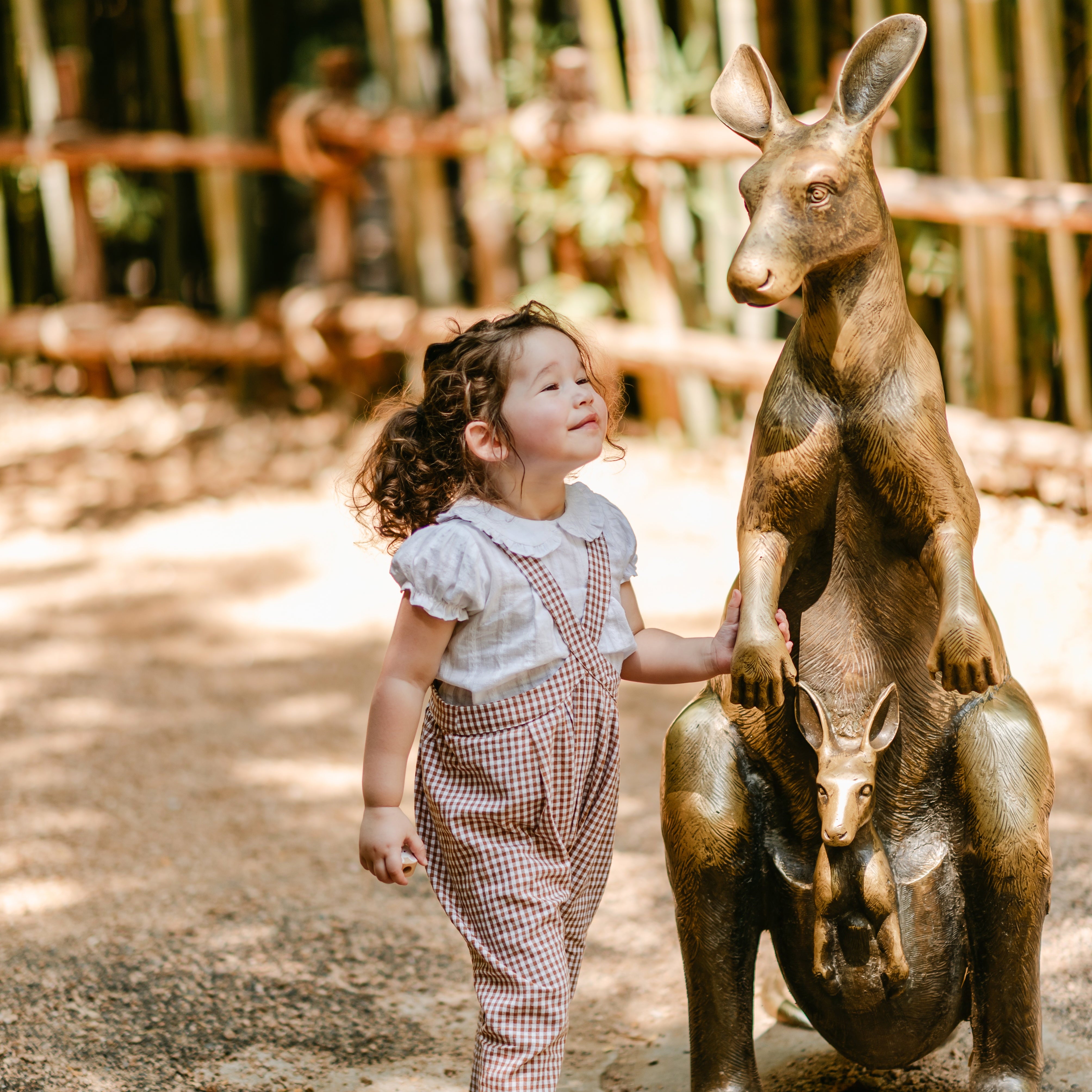 Child interacting with a kangaroo statue in an outdoor setting with bamboo in the background