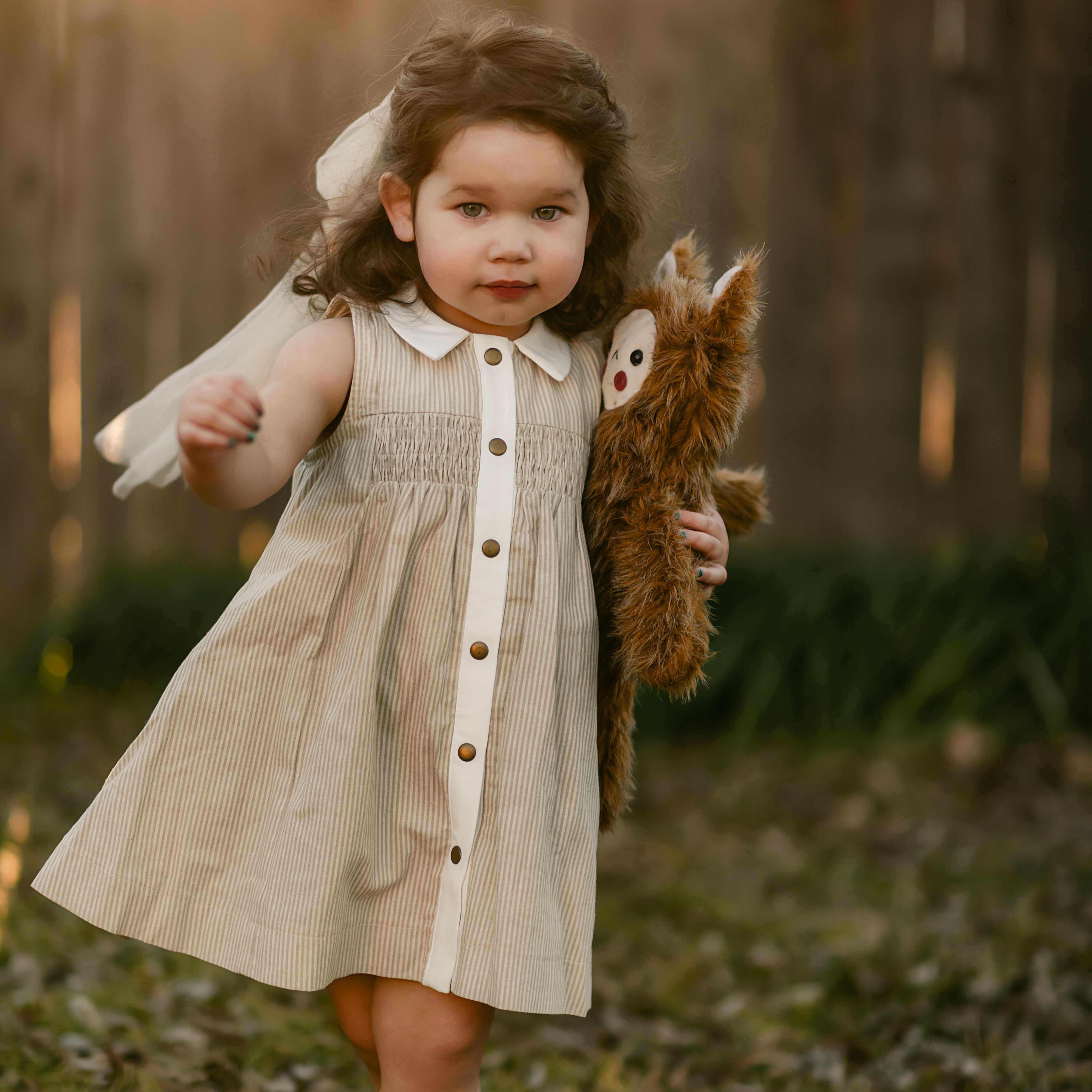 girl in a beige striped dress walking with toy monster