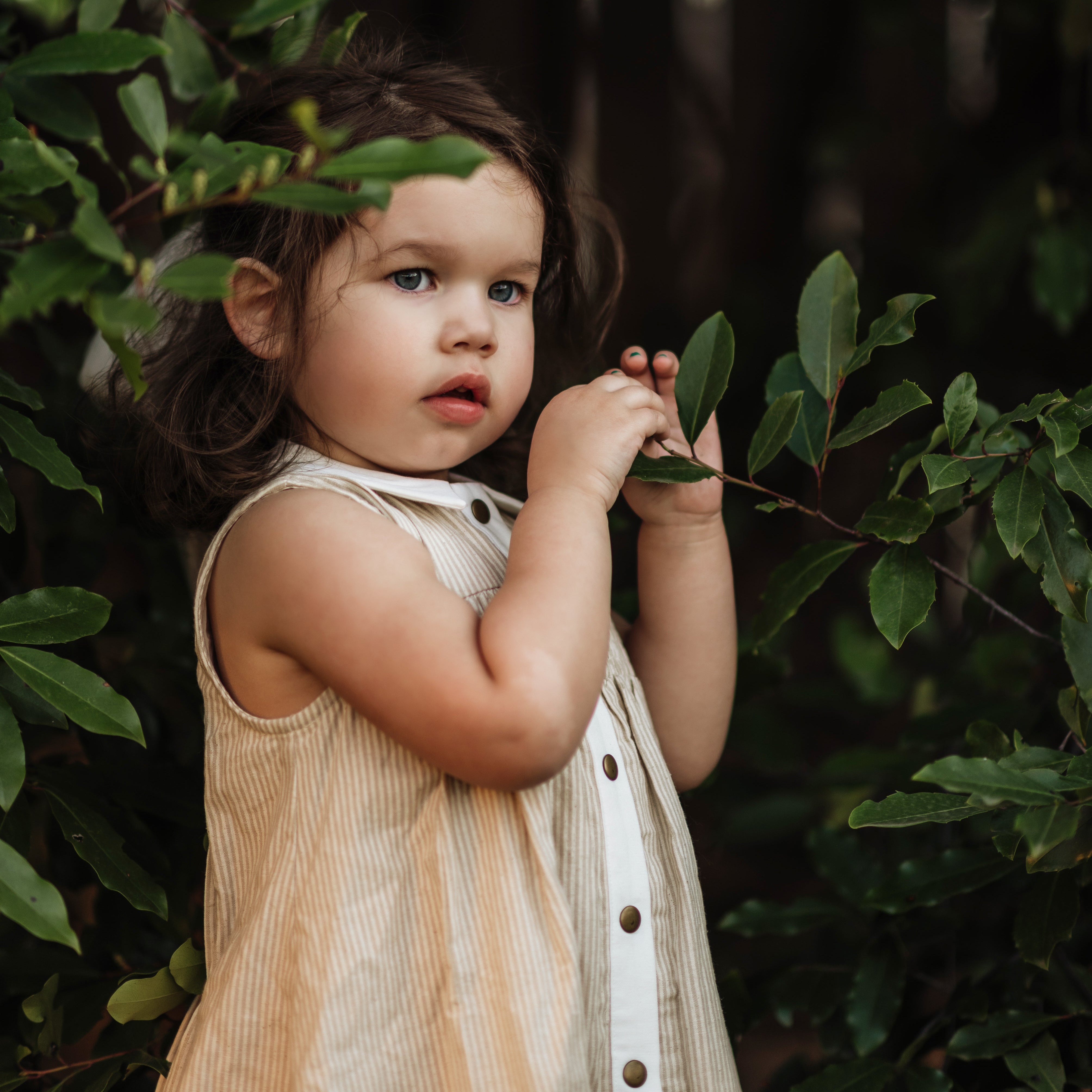 girl in a beige striped dress holding plants