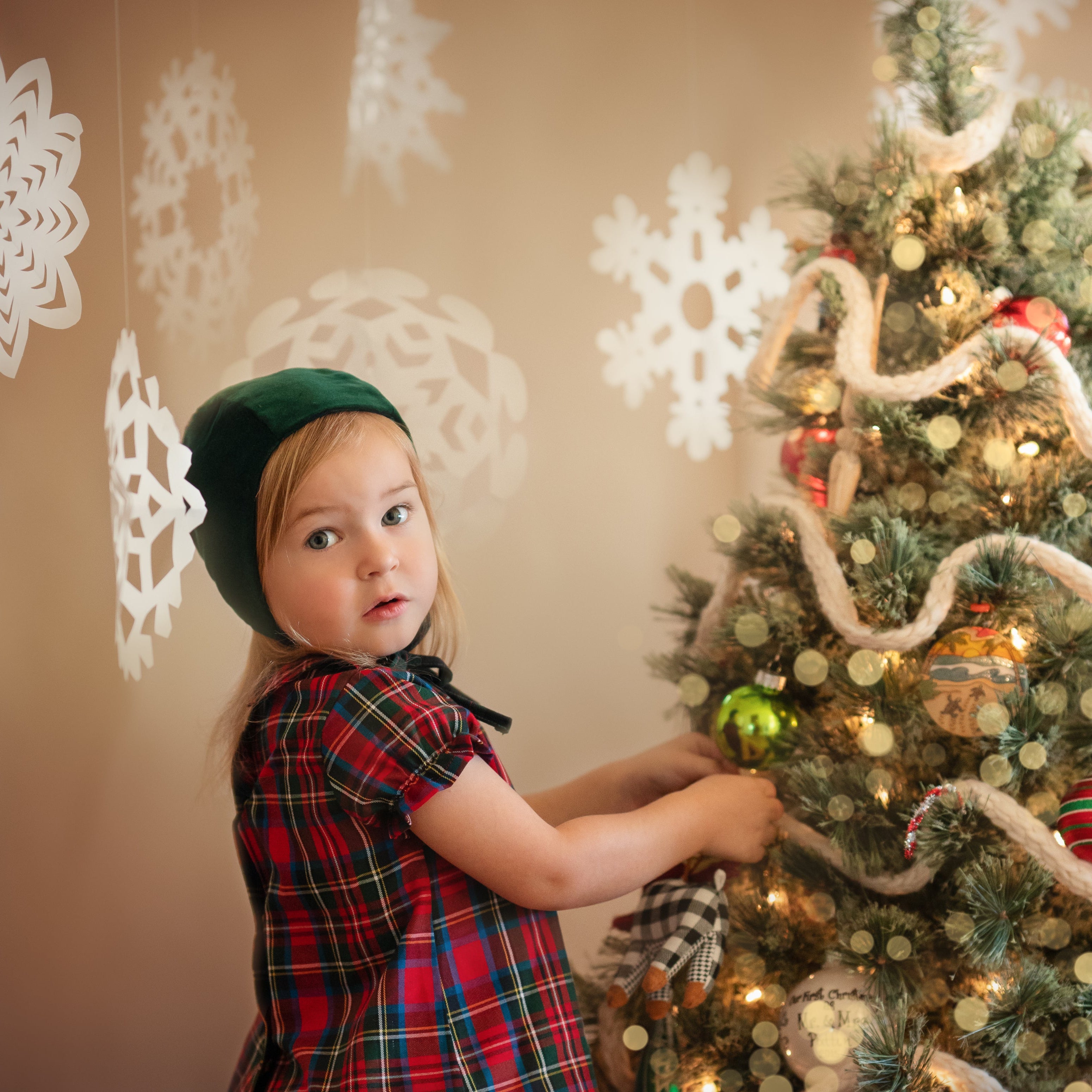 Girl in green bonnet and plaid blouse decorating a Xmas tree