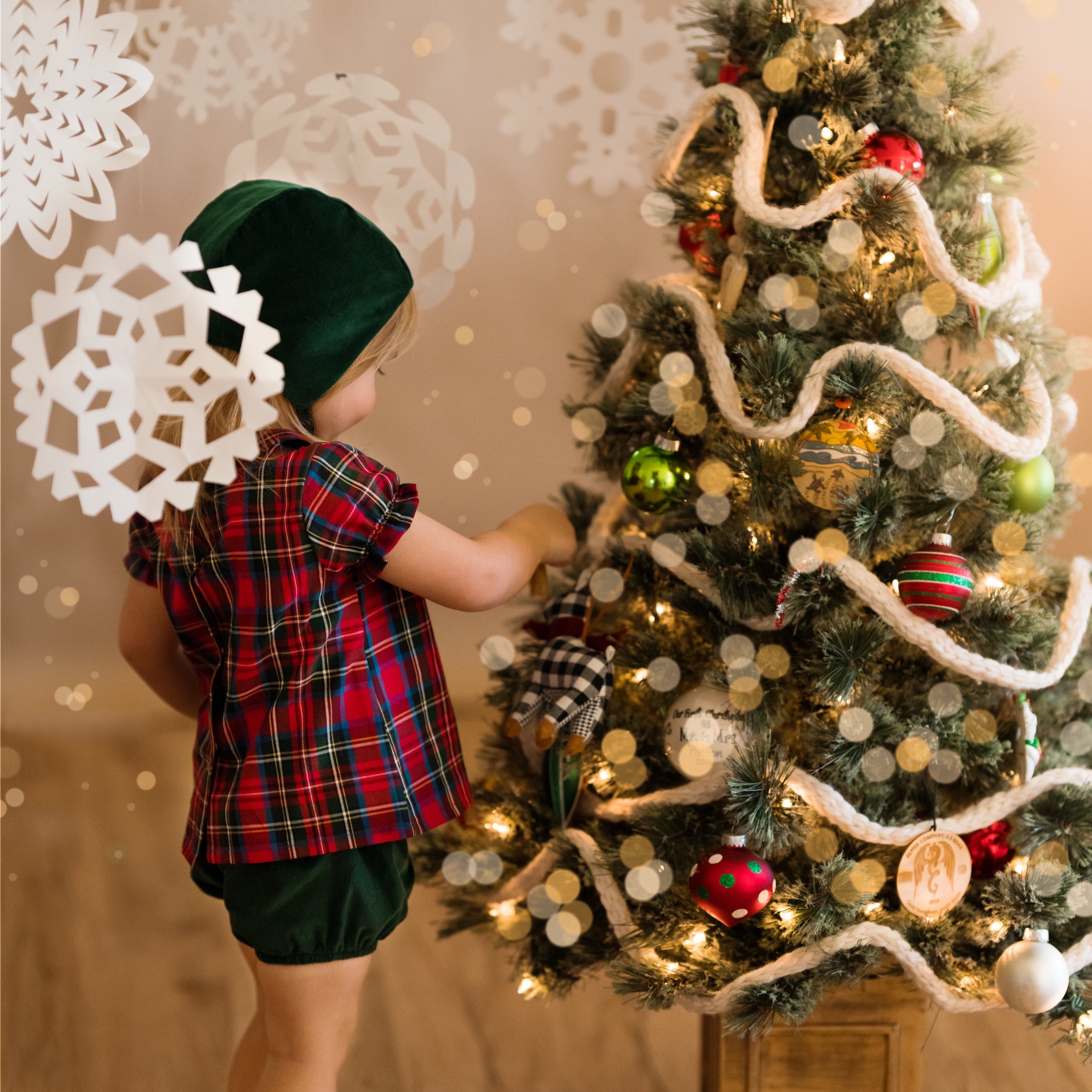 Girl in green bonnet and plaid blouse decorating a Xmas tree