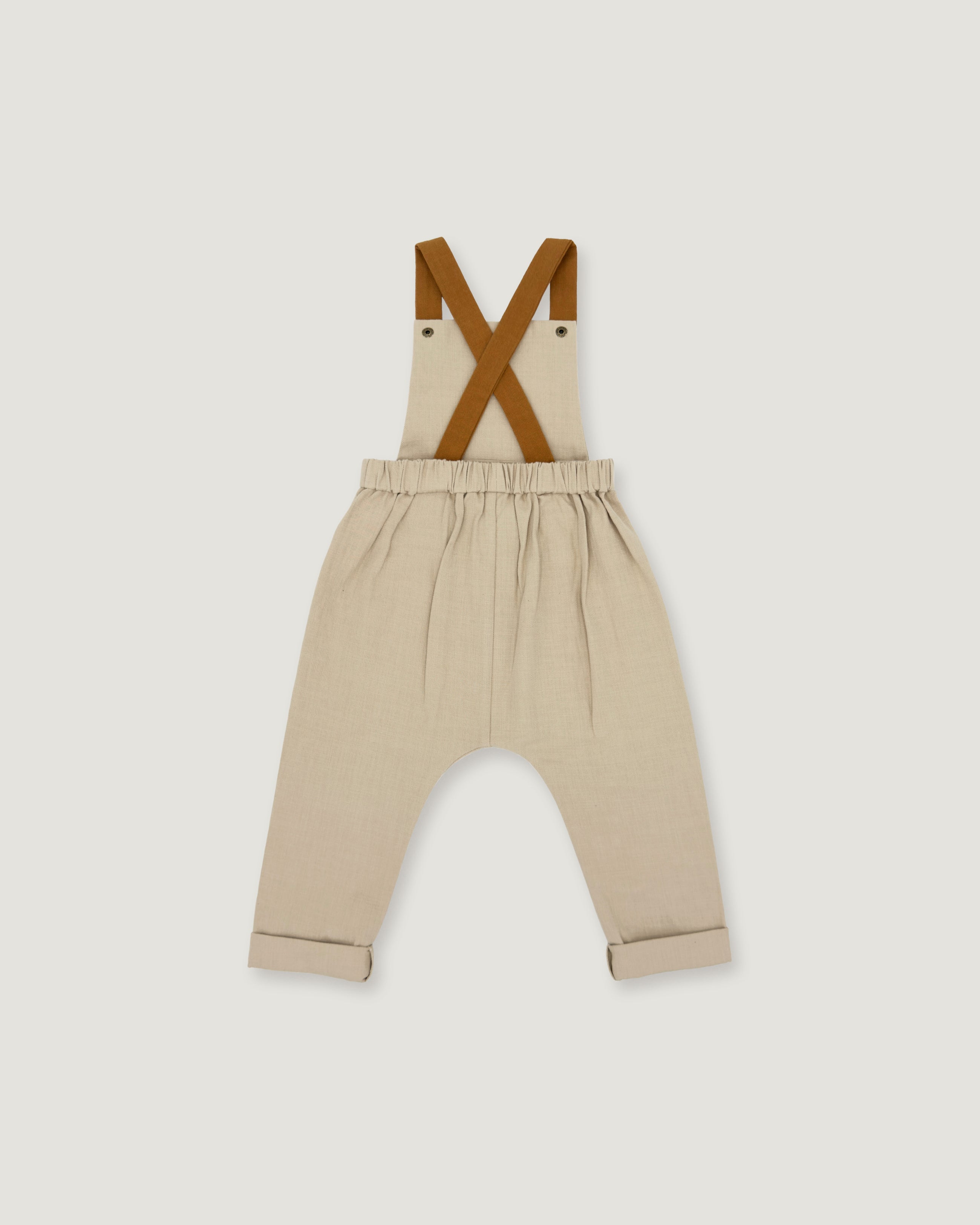 A pair of beige toddler pants with brown suspenders, laid flat against a light gray background.