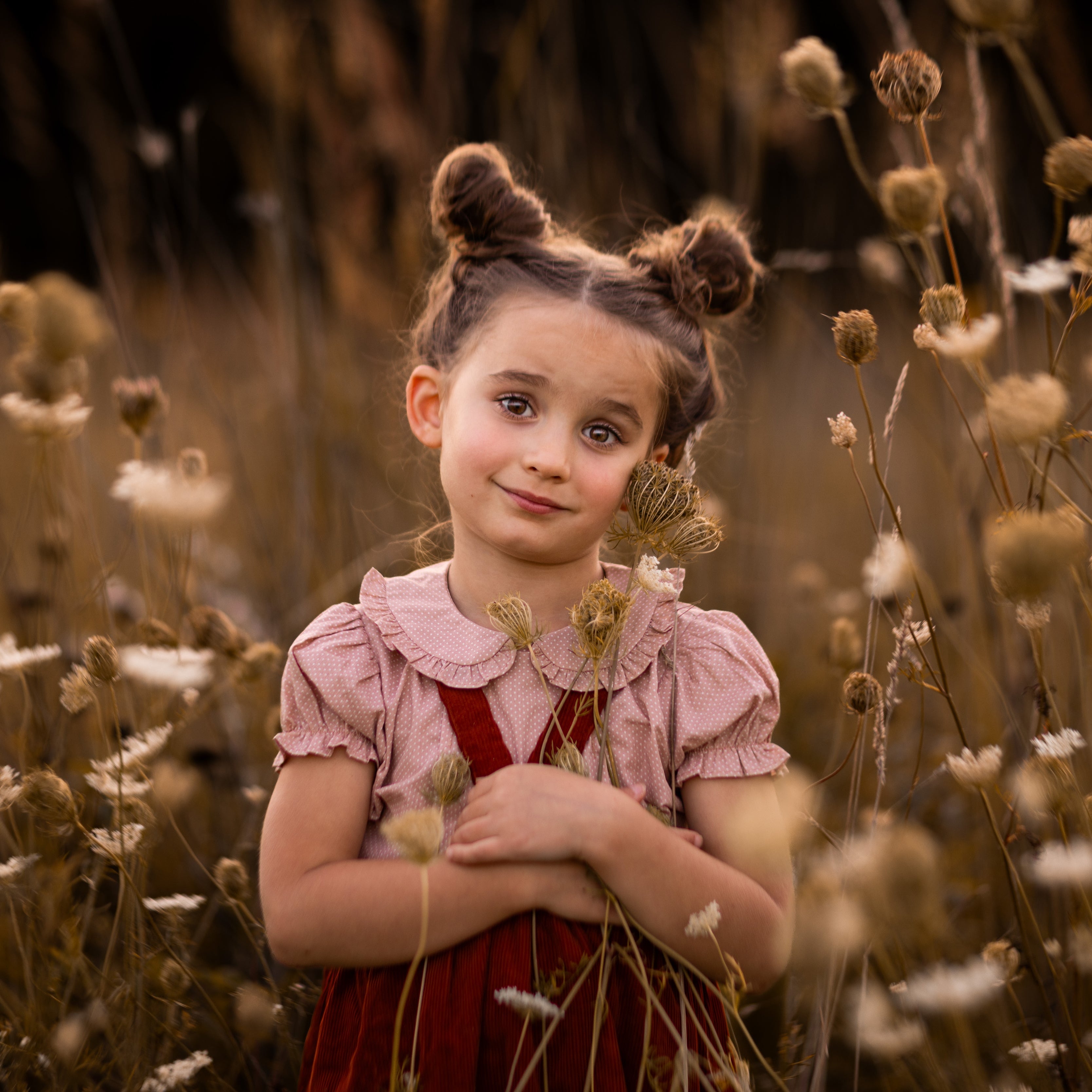 Young girl in a red dress standing among tall grass and wildflowers