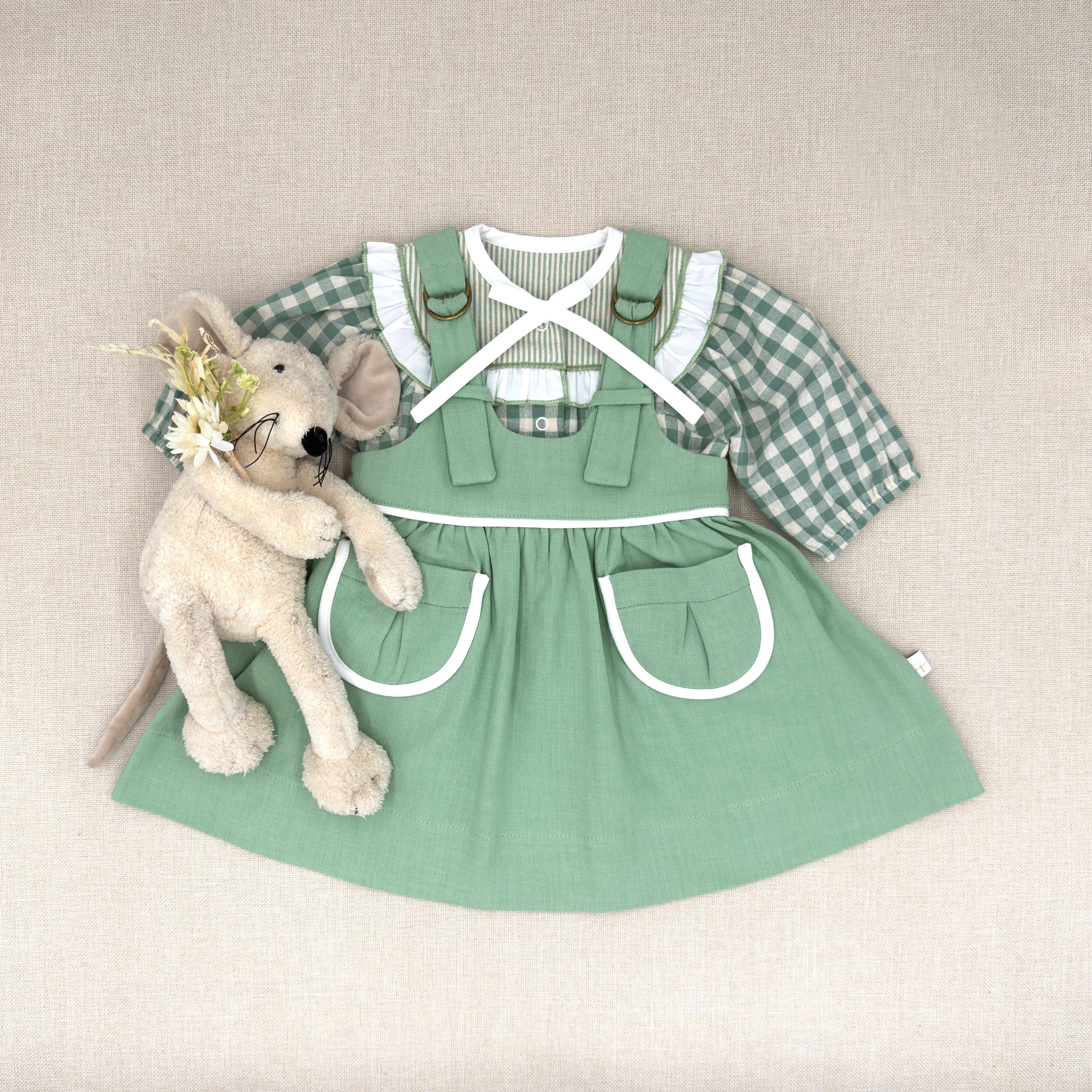 Green dress with overalls and plaid shirt on a neutral background