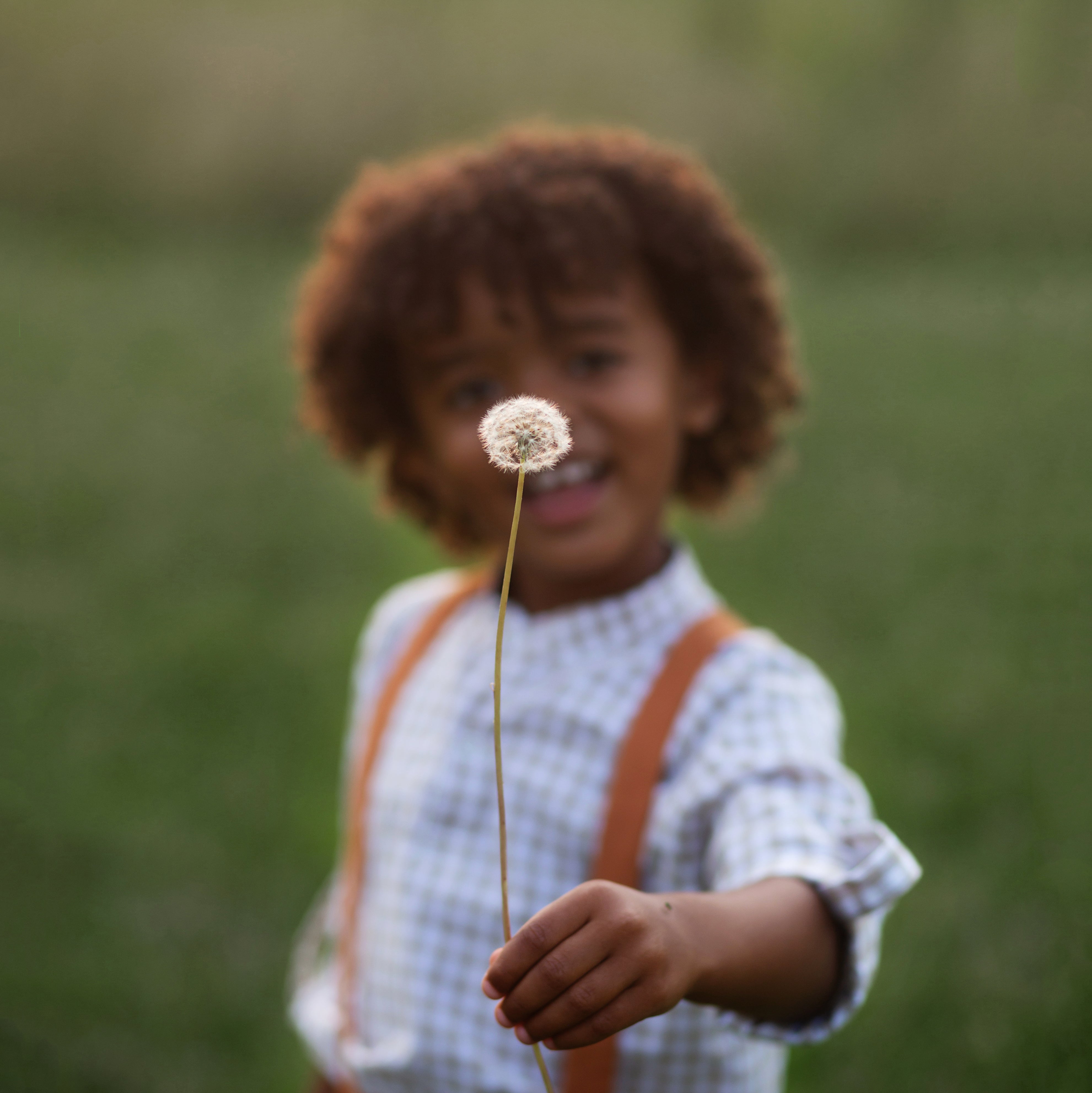 Playful image of Beige Gingham Henley Shirt worn by 5-year-old boy in size 5Y, featuring a classic Henley placket and 3/4 cuffed sleeves that can be unrolled for layering. Paired with burnt orange linen suspender shorts for a stylish, versatile outfit.