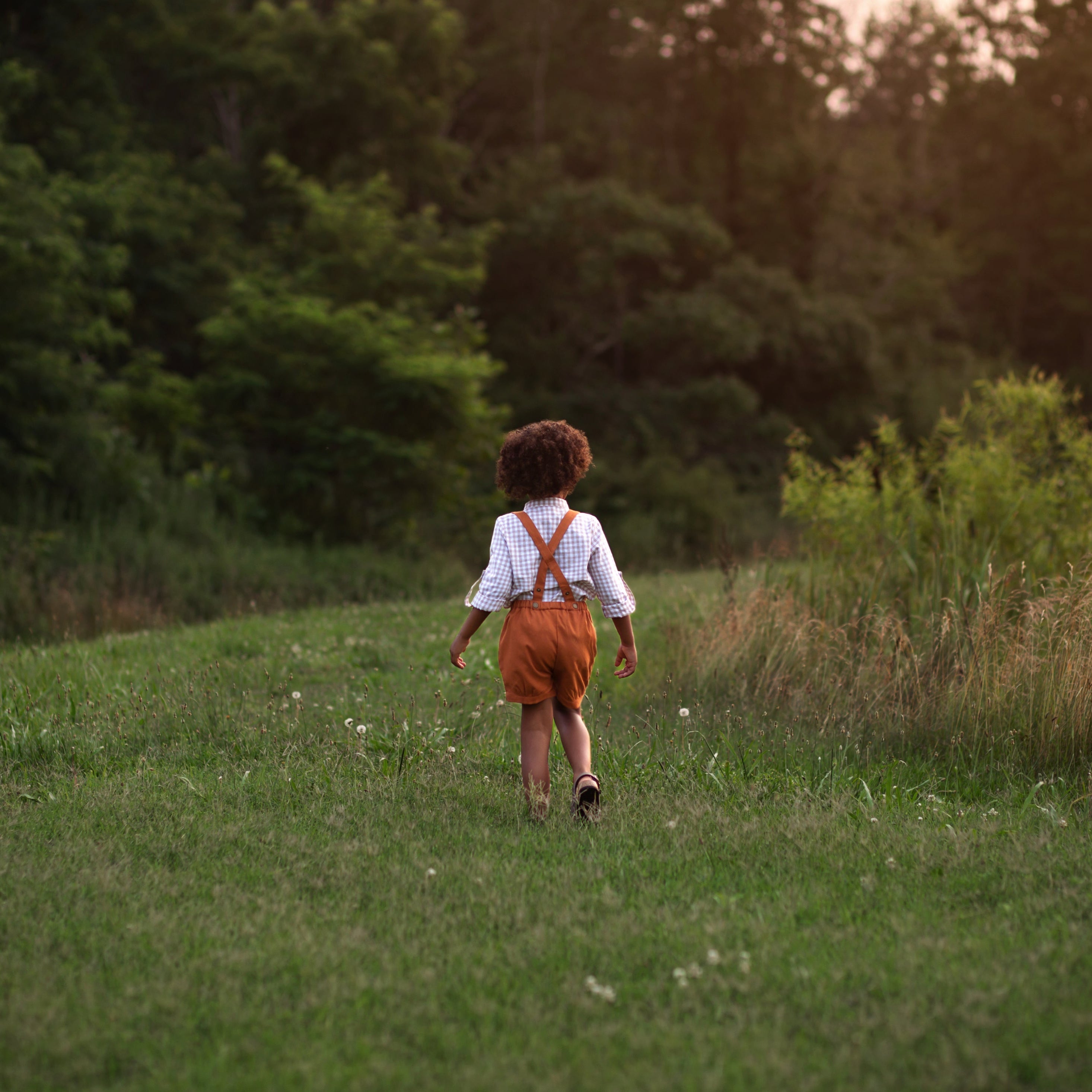 Model boy wearing the Burnt Orange Suspender Shorts with Beige Gingham Henley Shirt, back view - This image showcases the back of the outfit, highlighting the adjustable straps and how they complement the overall look.