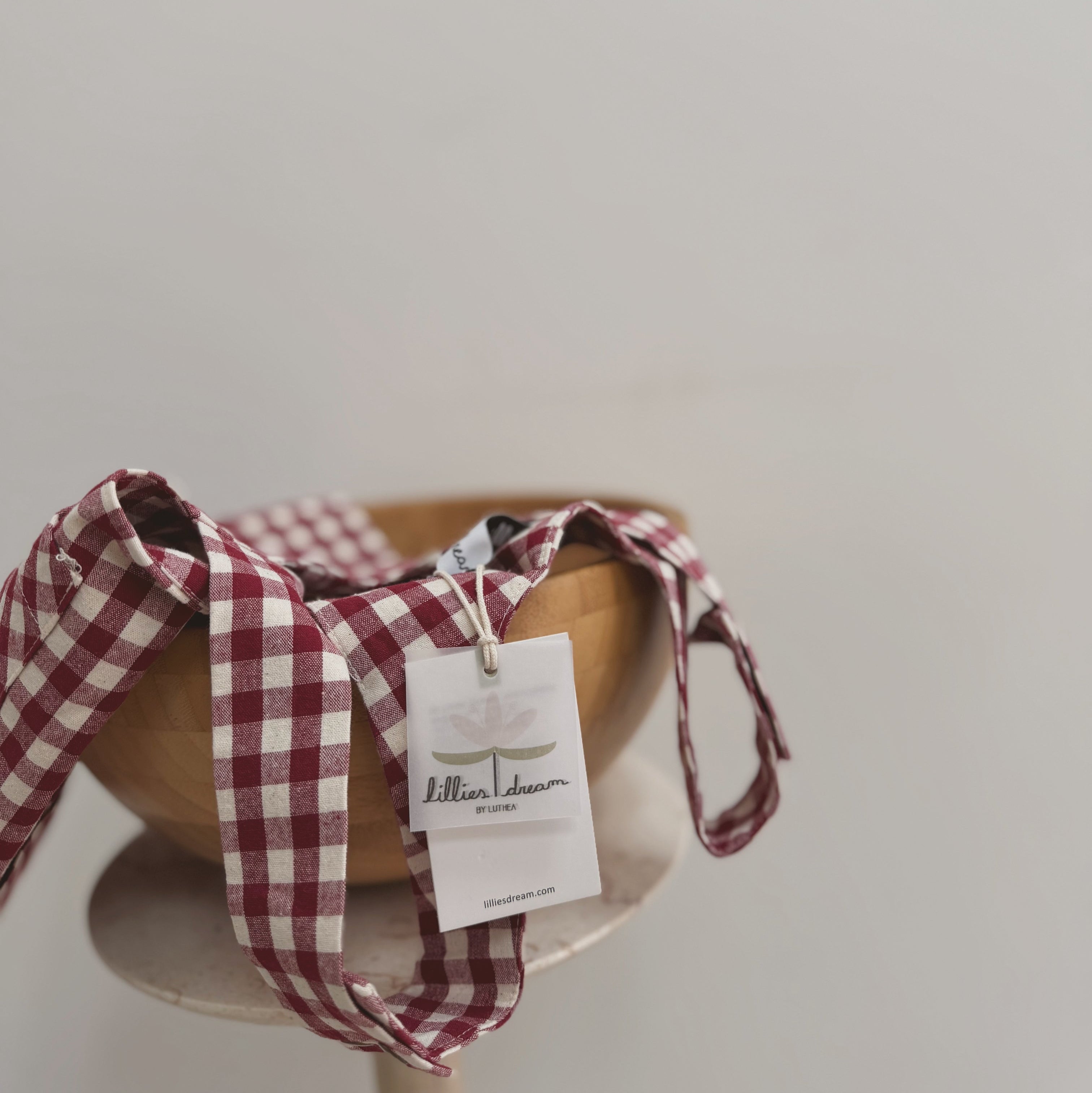 Wooden bowl with a red and white checkered ribbon and a tag on a light gray background