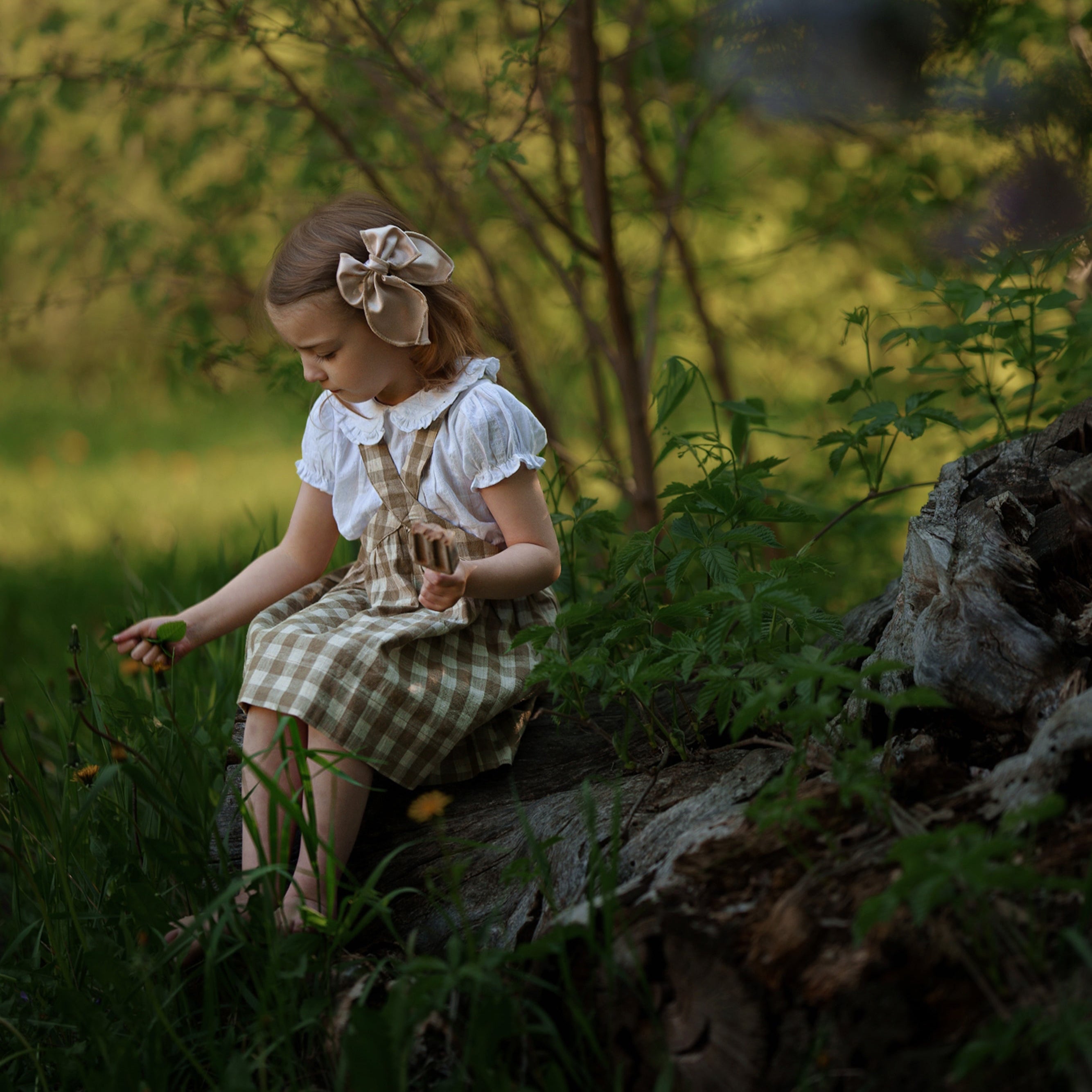 Young girl in a checkered dress sitting on a log in a forest setting