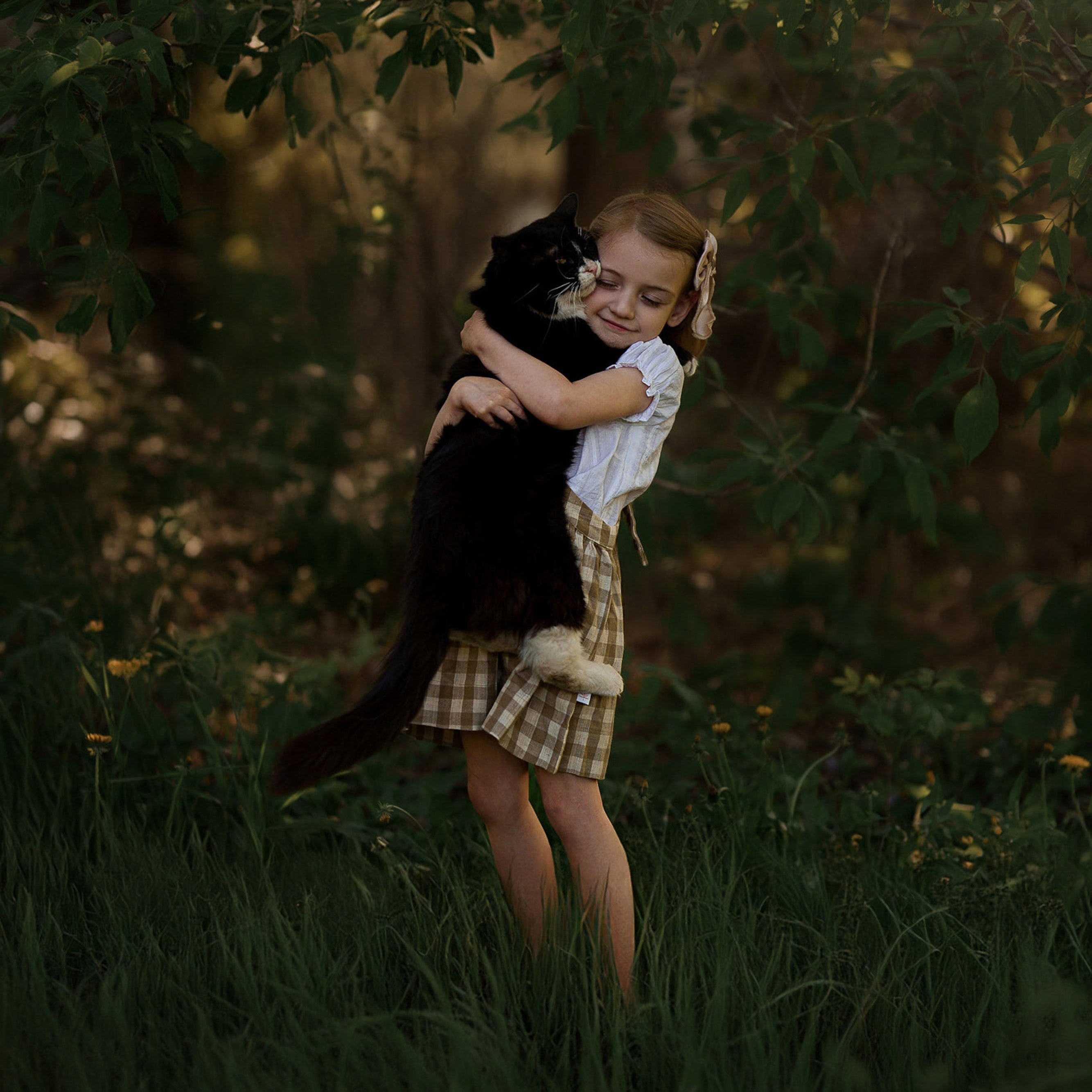 Young girl holding a black cat in a forest setting