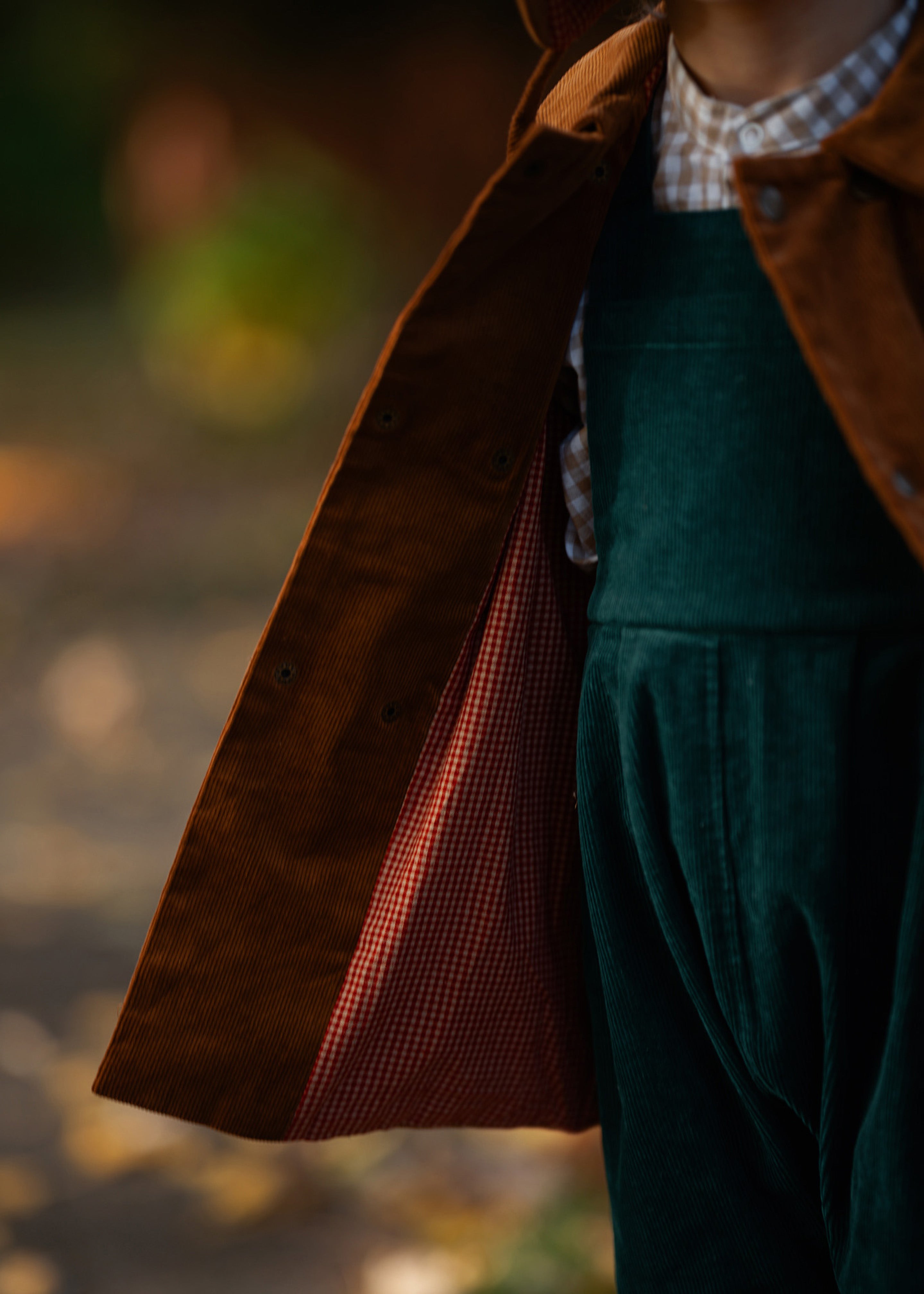 Person wearing a brown coat and green overalls with a blurred background