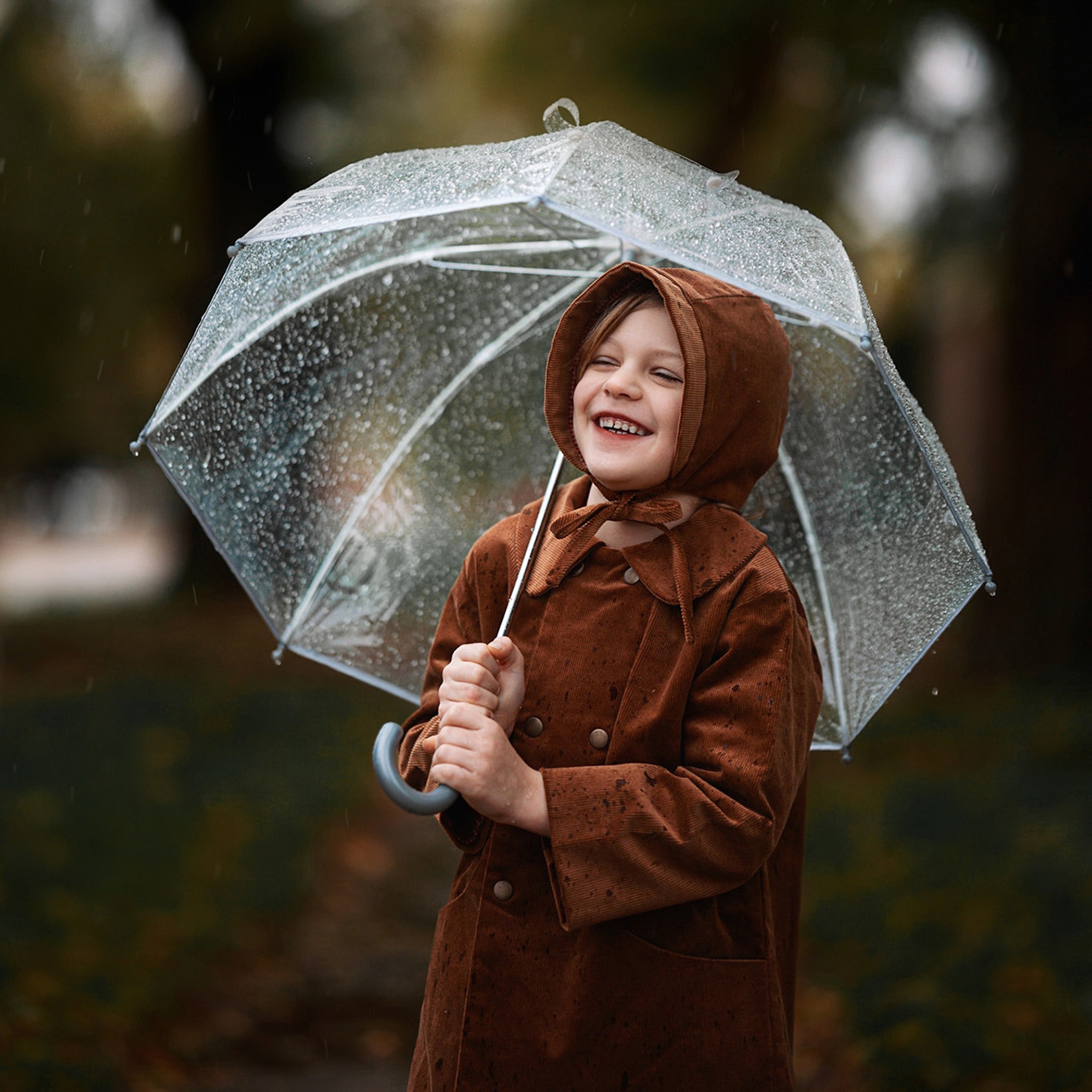 Under the Rain with Umbrella: The boy, sheltered under an umbrella, demonstrates the coat’s functionality in wet weather, looking fashionable and cozy in natural materials.