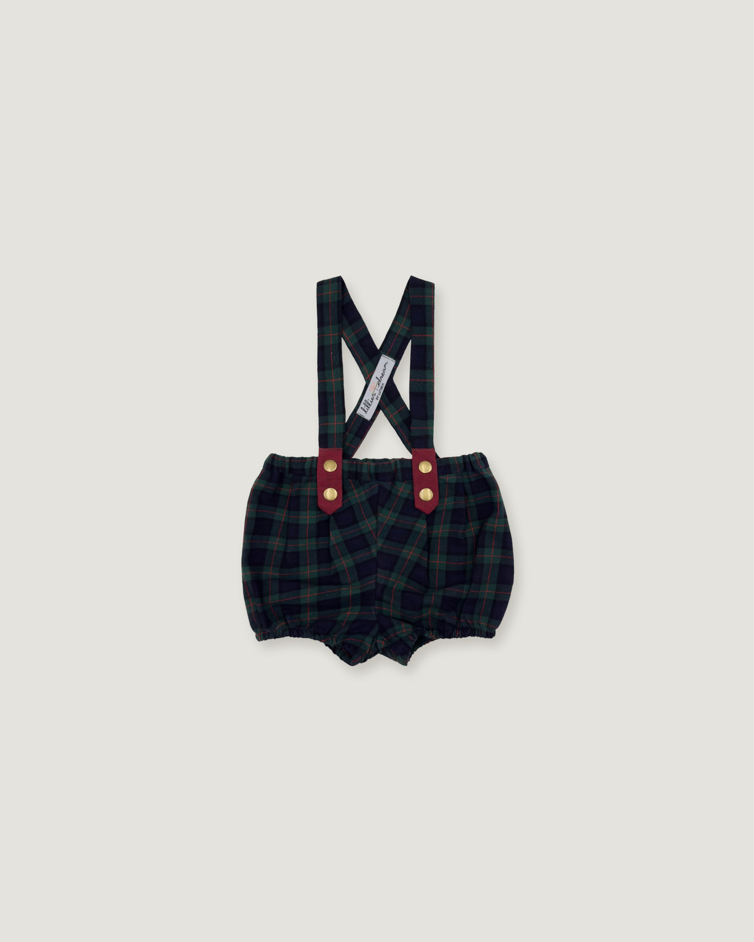 A pair of baby boy's plaid bib shorts with suspenders, featuring a dark green and black checkered pattern, red button accents, and a white brand tag on the suspenders, shown against a solid light gray background.