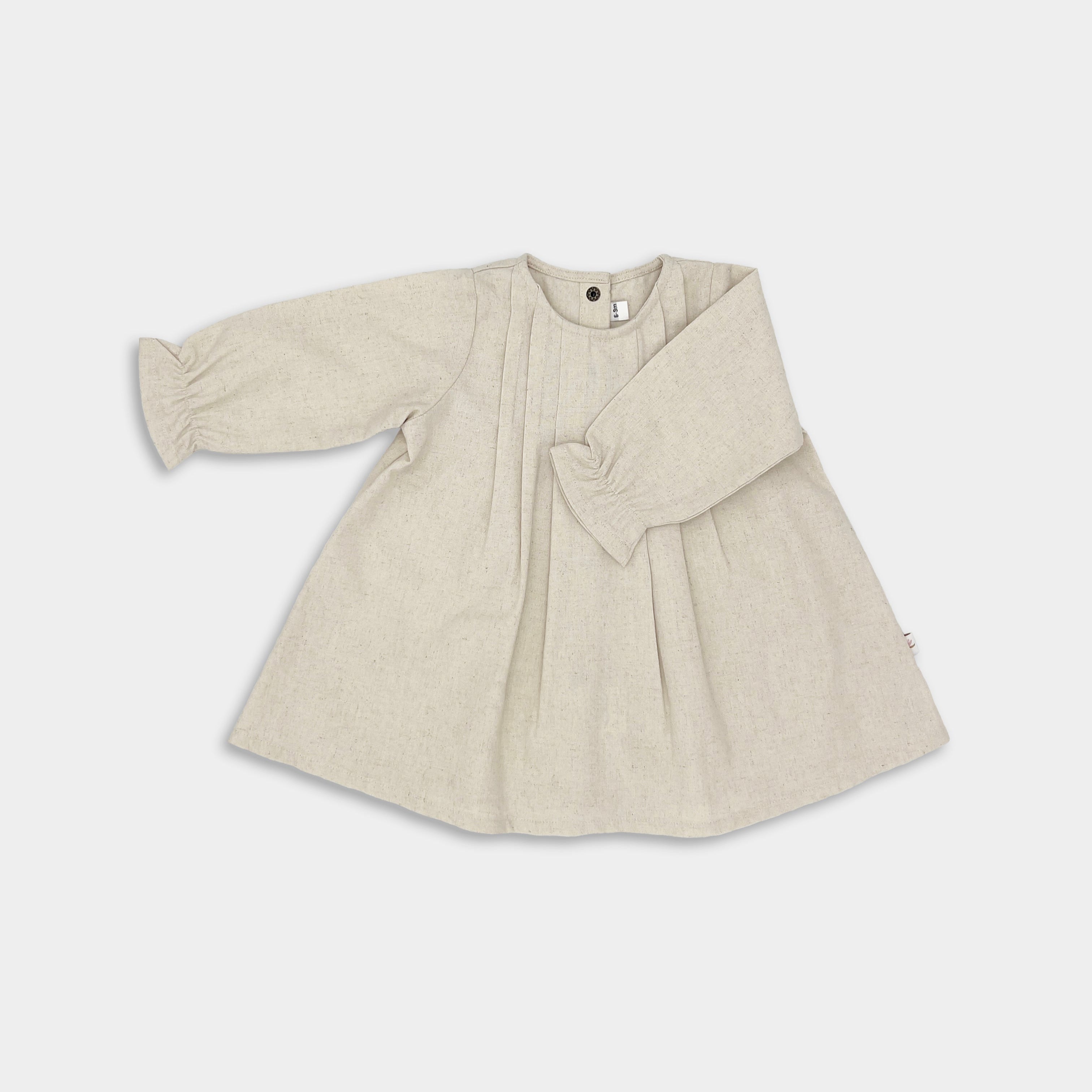 A natural long sleeve dress for girls, with pin-tucked details, pleated back yoke, and ruffled hem.