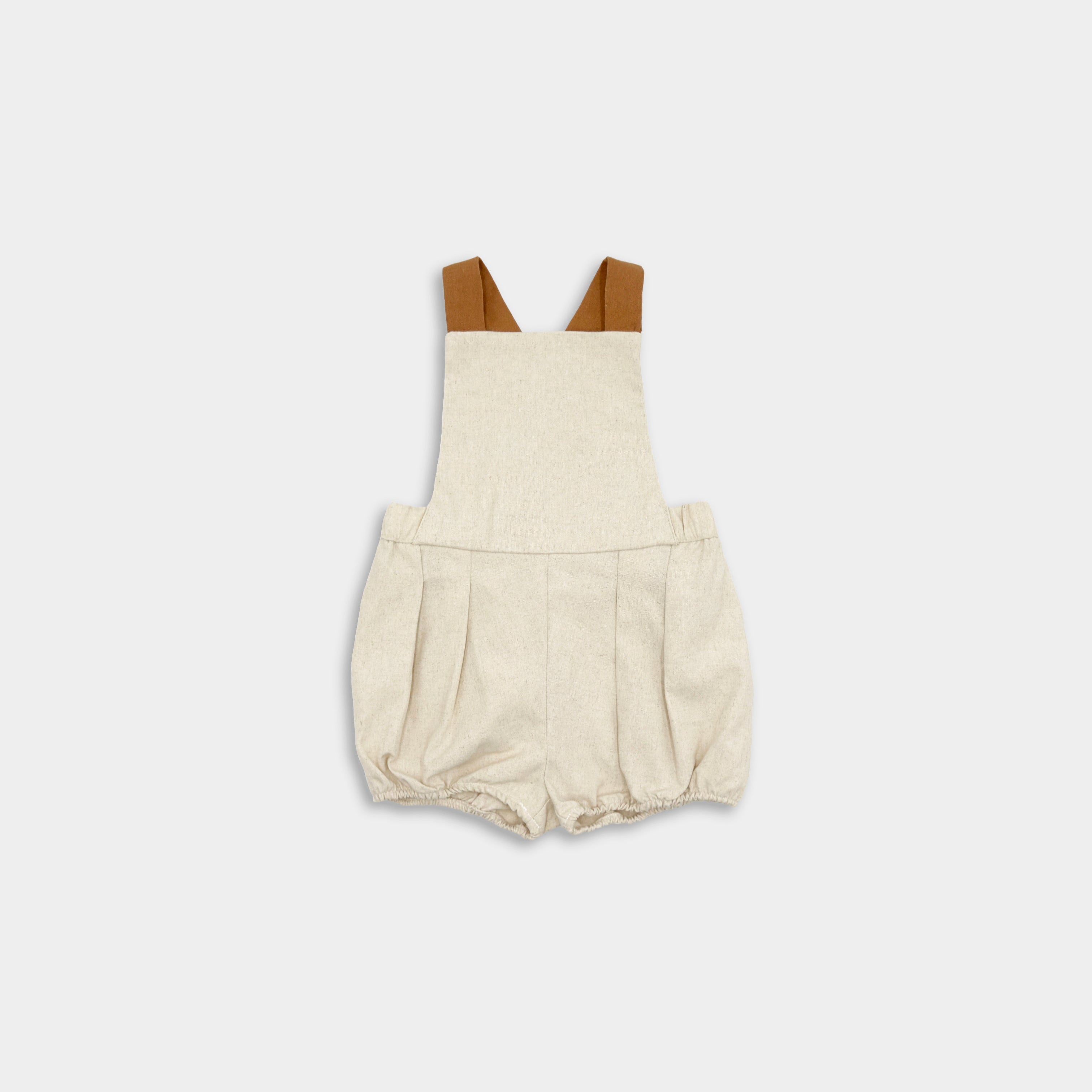 A beige linen bubble romper for children, with adjustable straps and elasticized legs.