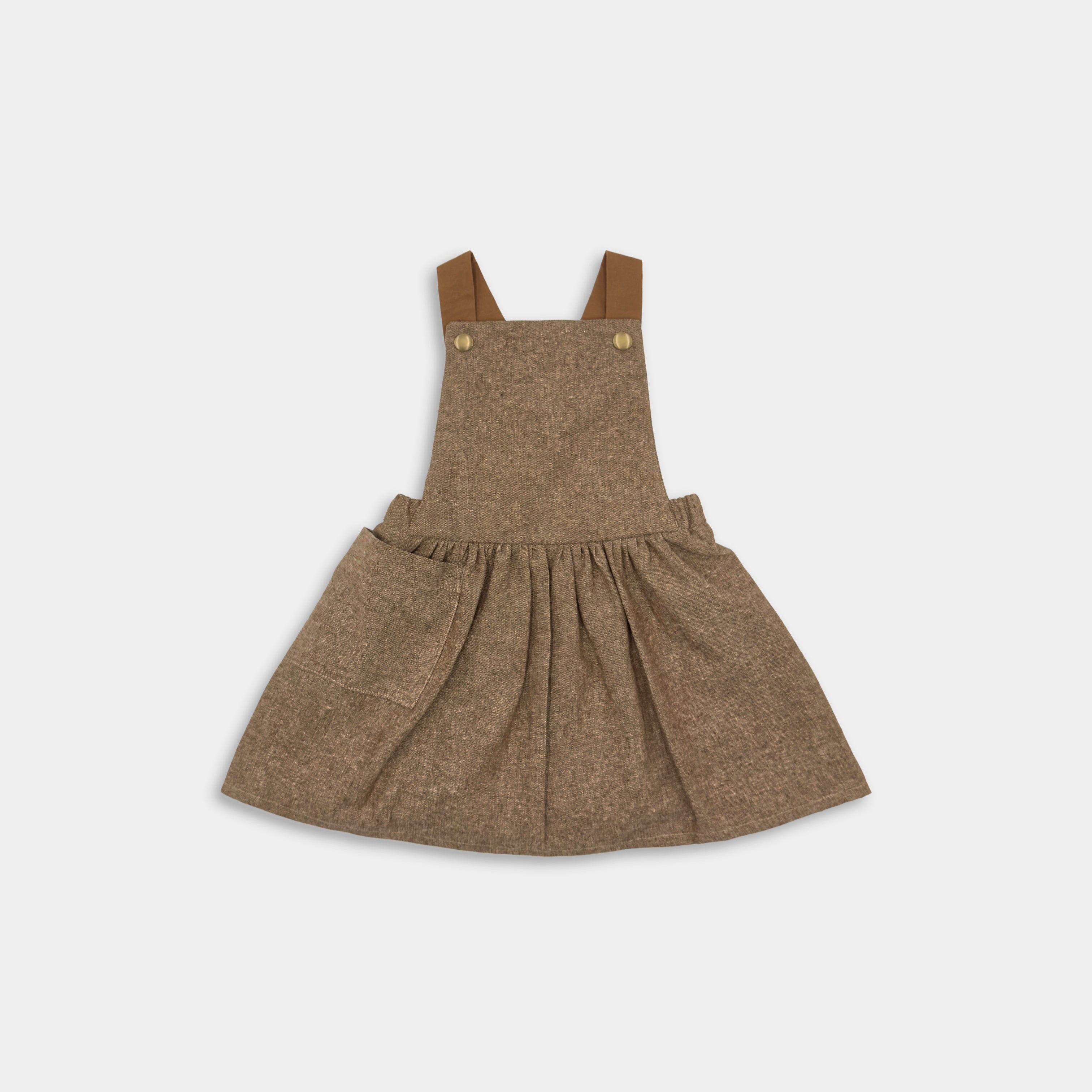 A nutmeg brown linen pinafore with adjustable leather-look straps and a large front pocket, on a white background.