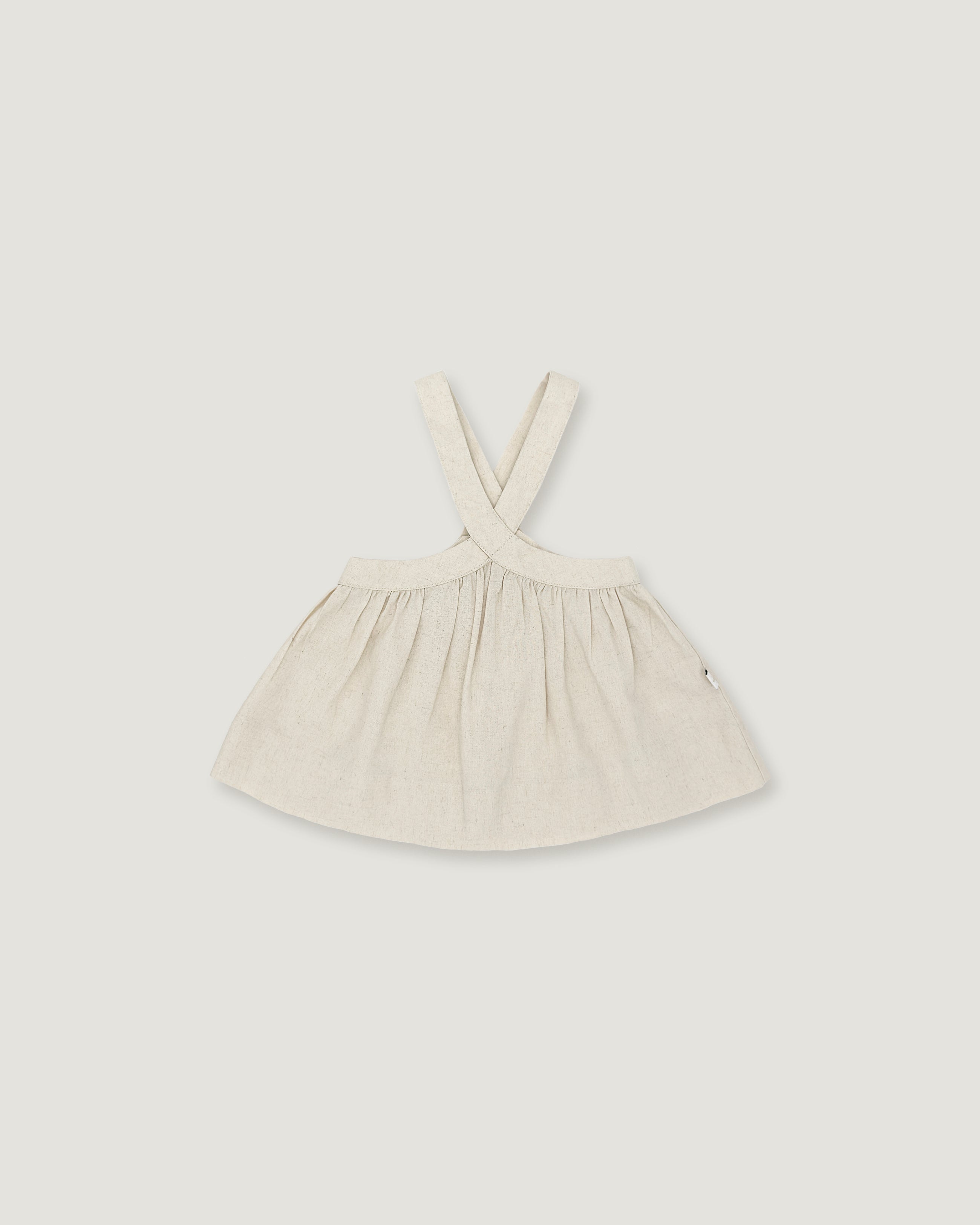 A light cream-colored linen dress with shoulder straps, laid flat against a neutral light gray background.