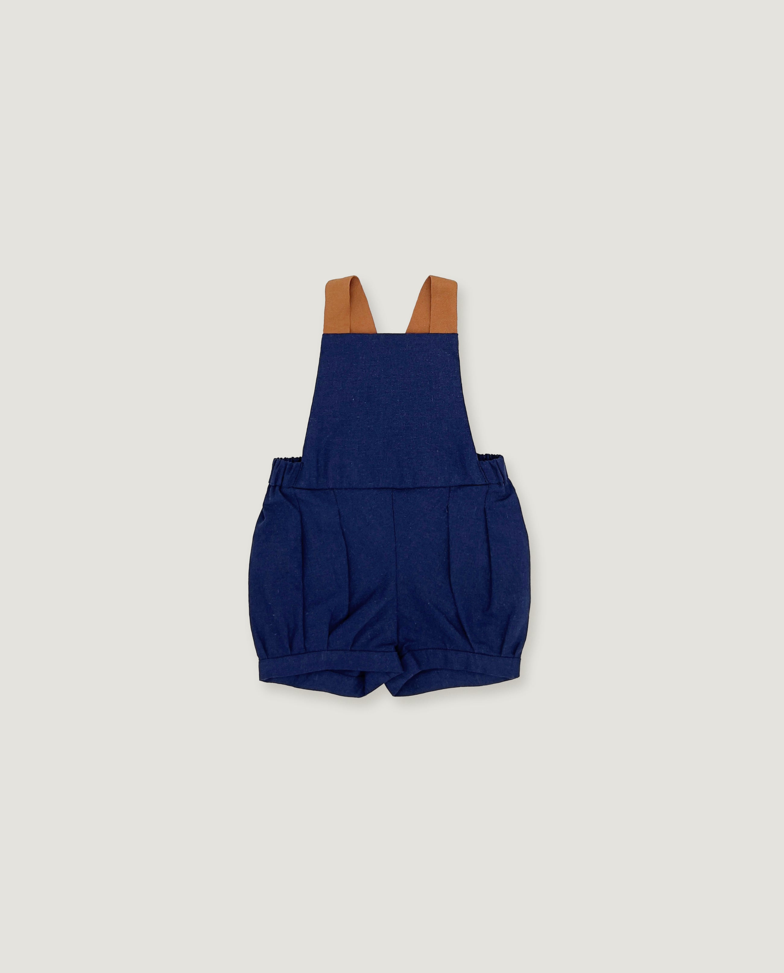 A pair of navy blue baby shorts with adjustable brown shoulder straps, laid flat against a light gray background.