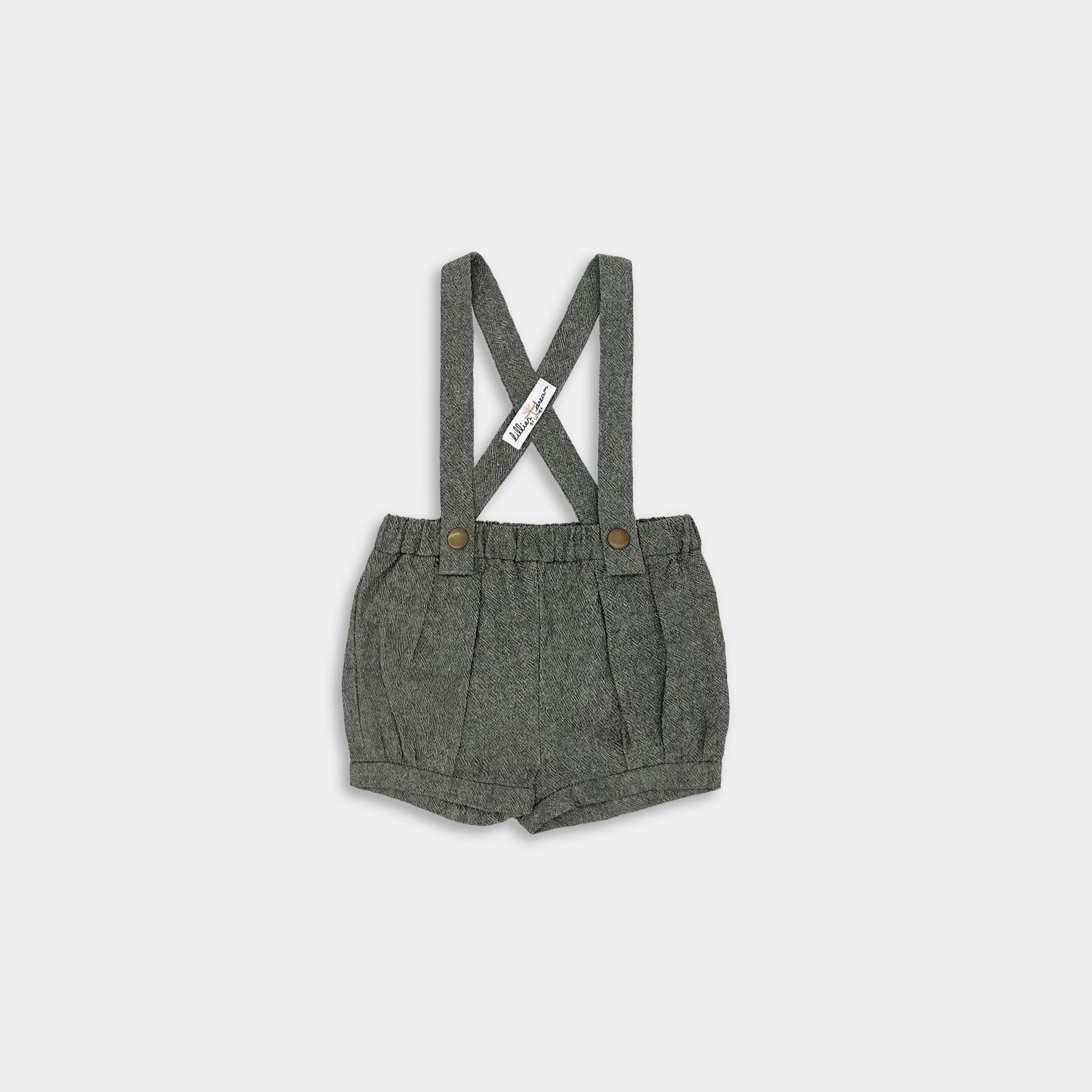 Olive green linen suspender shorts with adjustable straps, pleats, and cuffs, featuring a conveniently positioned label.