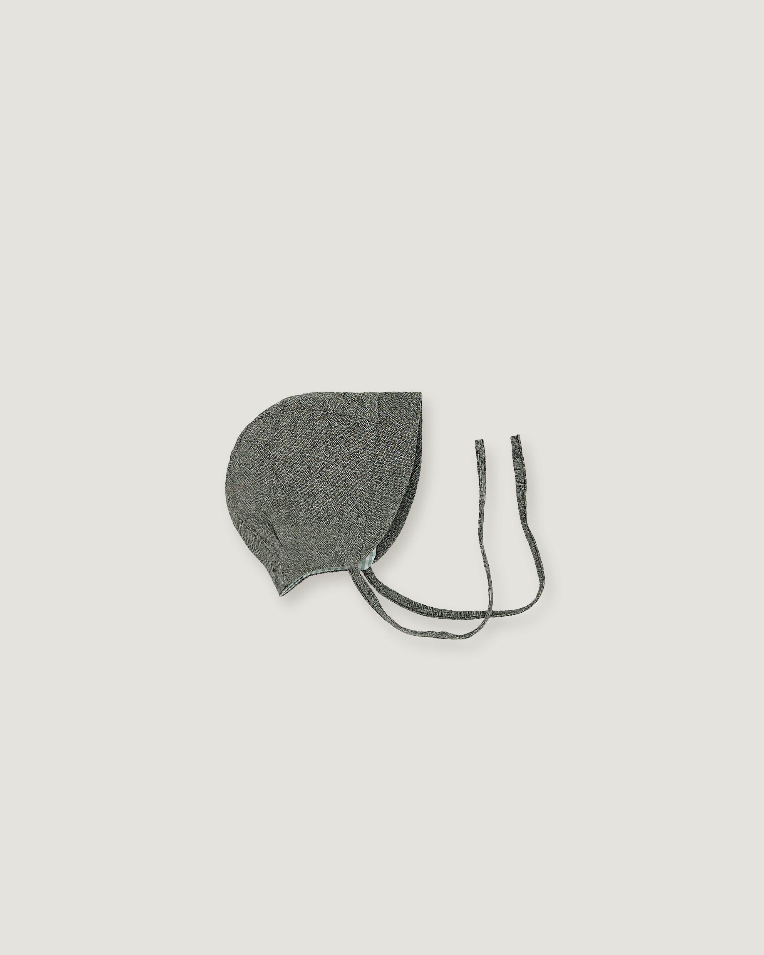 A green gray fabric bonnet with long ties, photographed flat against a solid light gray background.