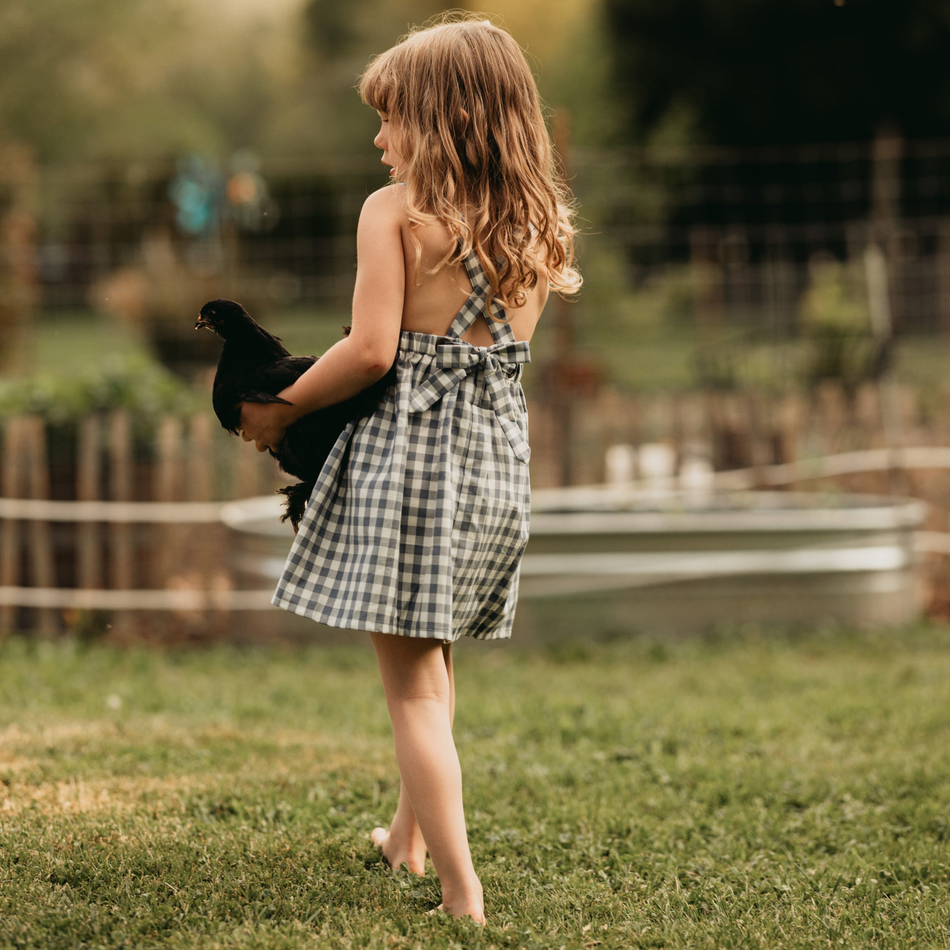 Back view of the model wearing a similar pinafore: The same 5-year-old model showcasing the back of the Slate Gingham pinafore, highlighting the strap design.