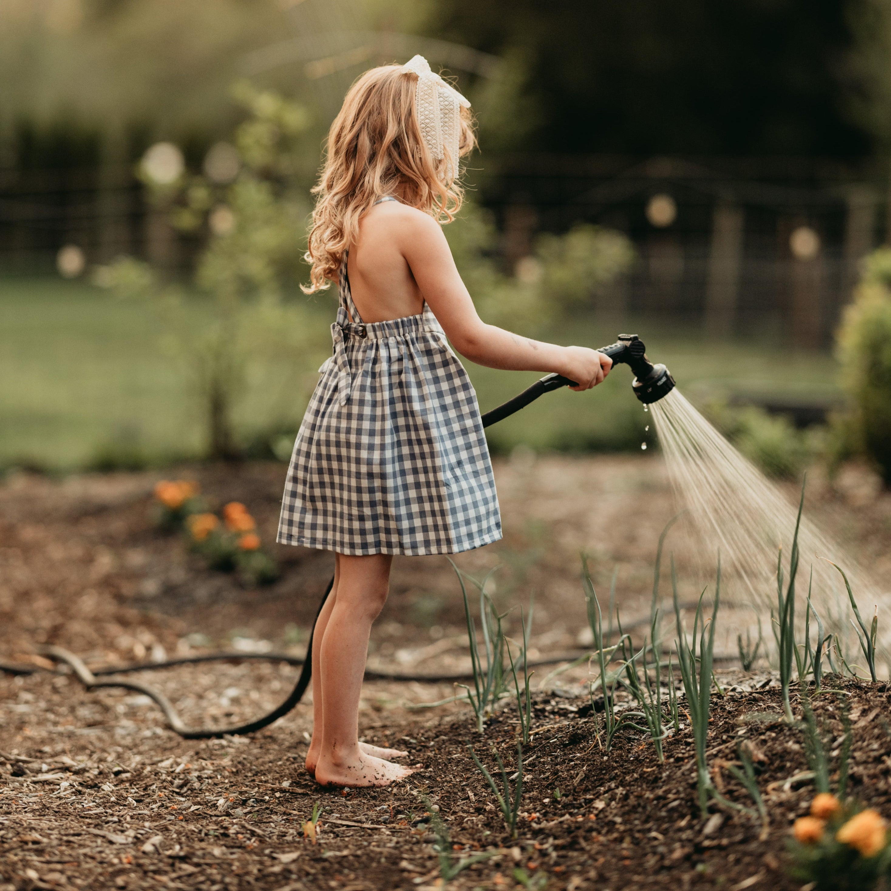 Side view of the model wearing a similar pinafore: A 5-year-old girl wearing a similar style pinafore in Slate Gingham, demonstrating the garment’s side profile and fit.