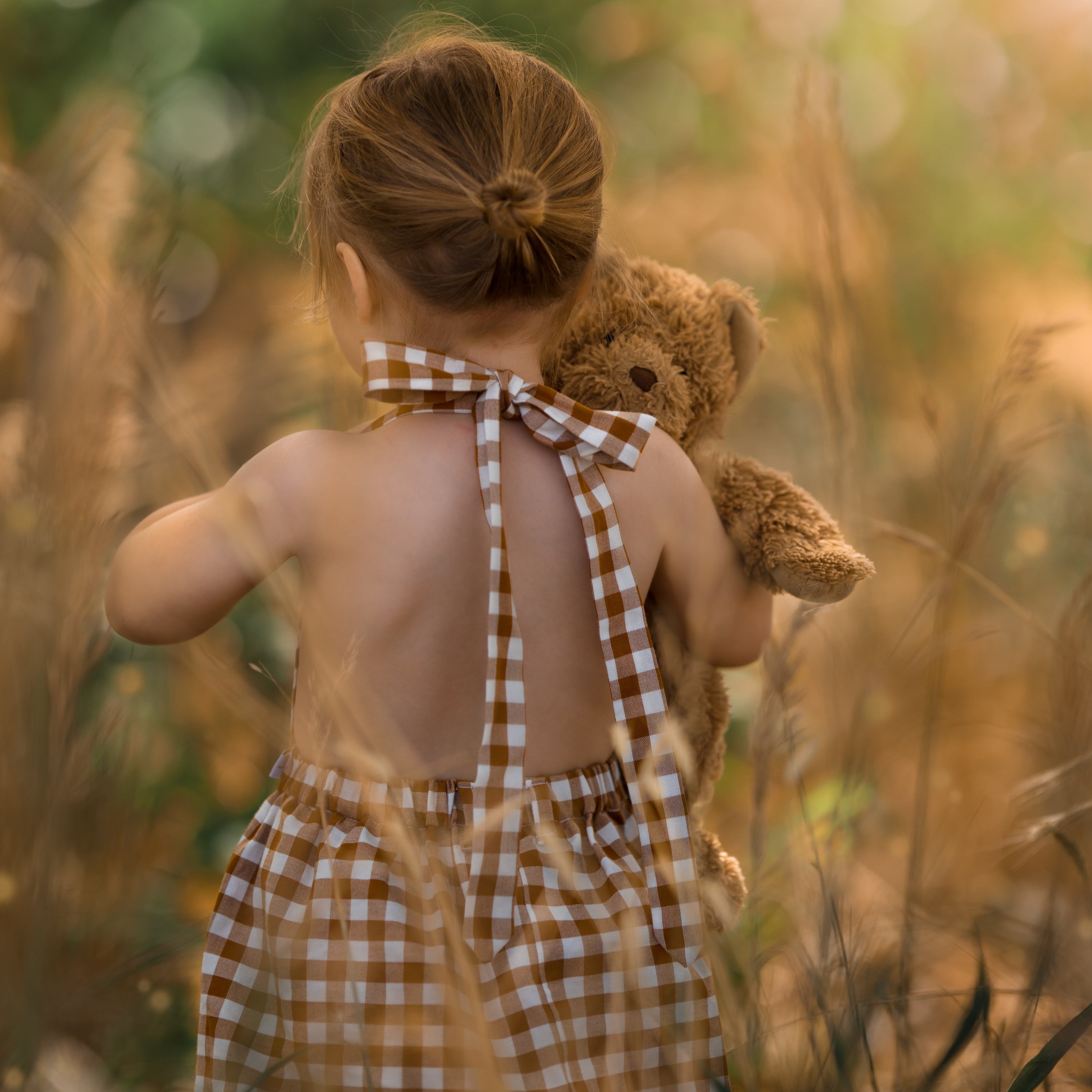 Model demonstrating alternative retro strap tying: A 3-year-old girl showing how to tie the straps of the Pinafore - Honey at the nape for a vintage-inspired look.