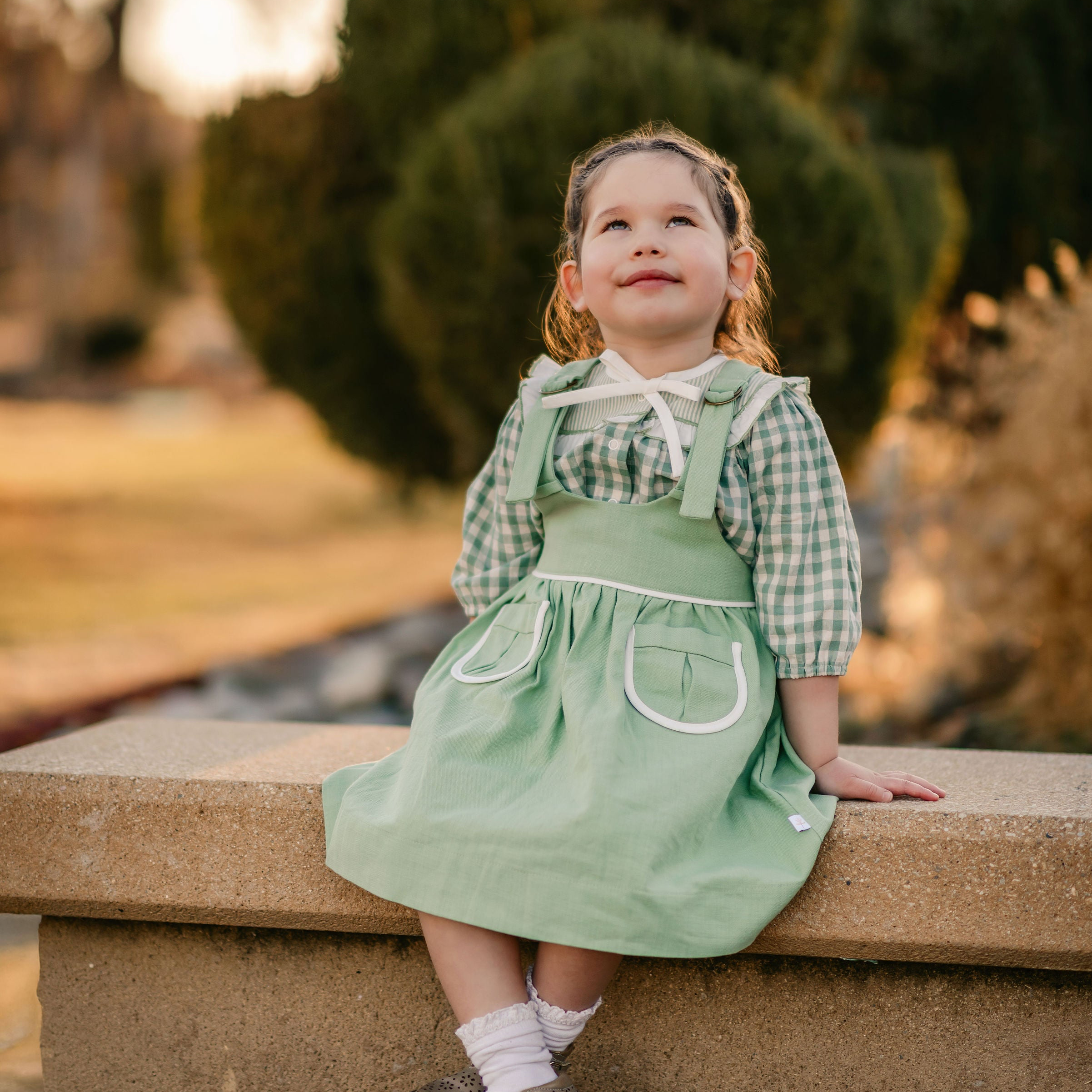 Young girl in a green dress sitting on a stone ledge outdoors.
