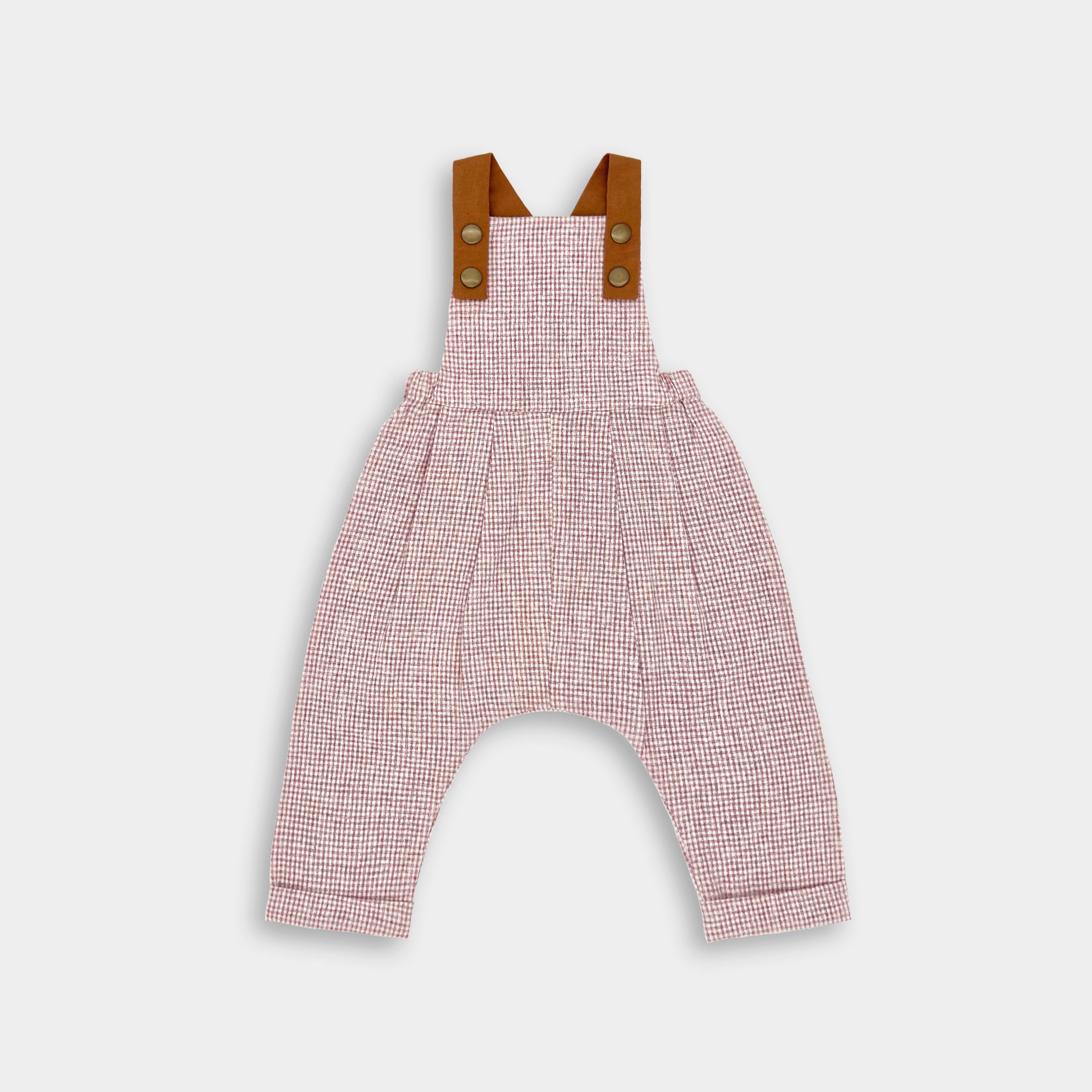 A pair of long overalls for children, featuring a rust gingham pattern, with leather-looking straps and pleats.