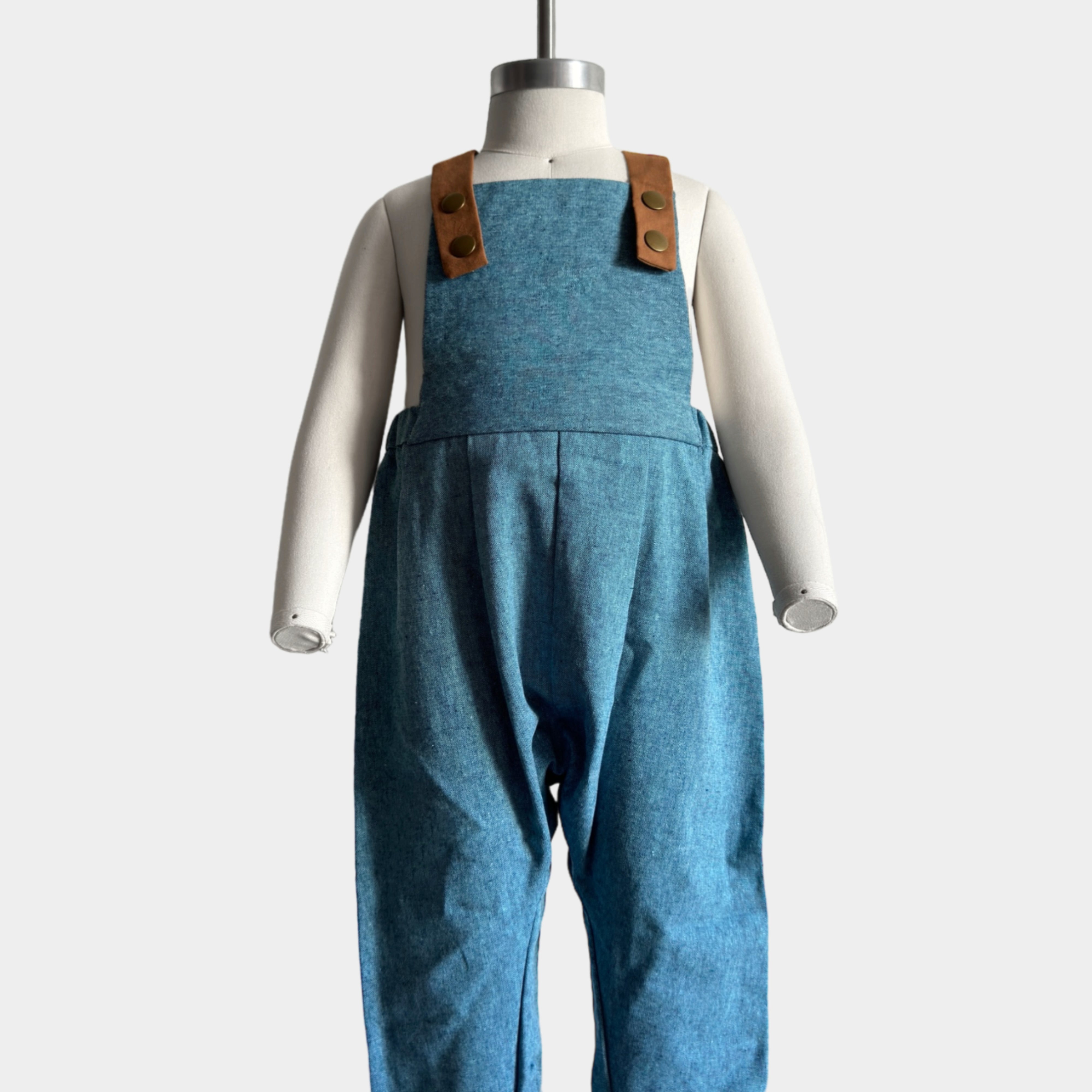 Blue Jay Long Overalls on a mannequin - Showcasing handmade overalls crafted from repurposed linen fabric, these gender-neutral pieces are perfect for passing down. The breathable fabric ensures comfort, while stylish pleats add elegance. Leather-looking straps enhance durability and visual appeal, and adjustable straps in two lengths provide a perfect fit. Unfoldable leg cuffs designed to grow with your little one make these overalls a versatile and sustainable wardrobe choice.