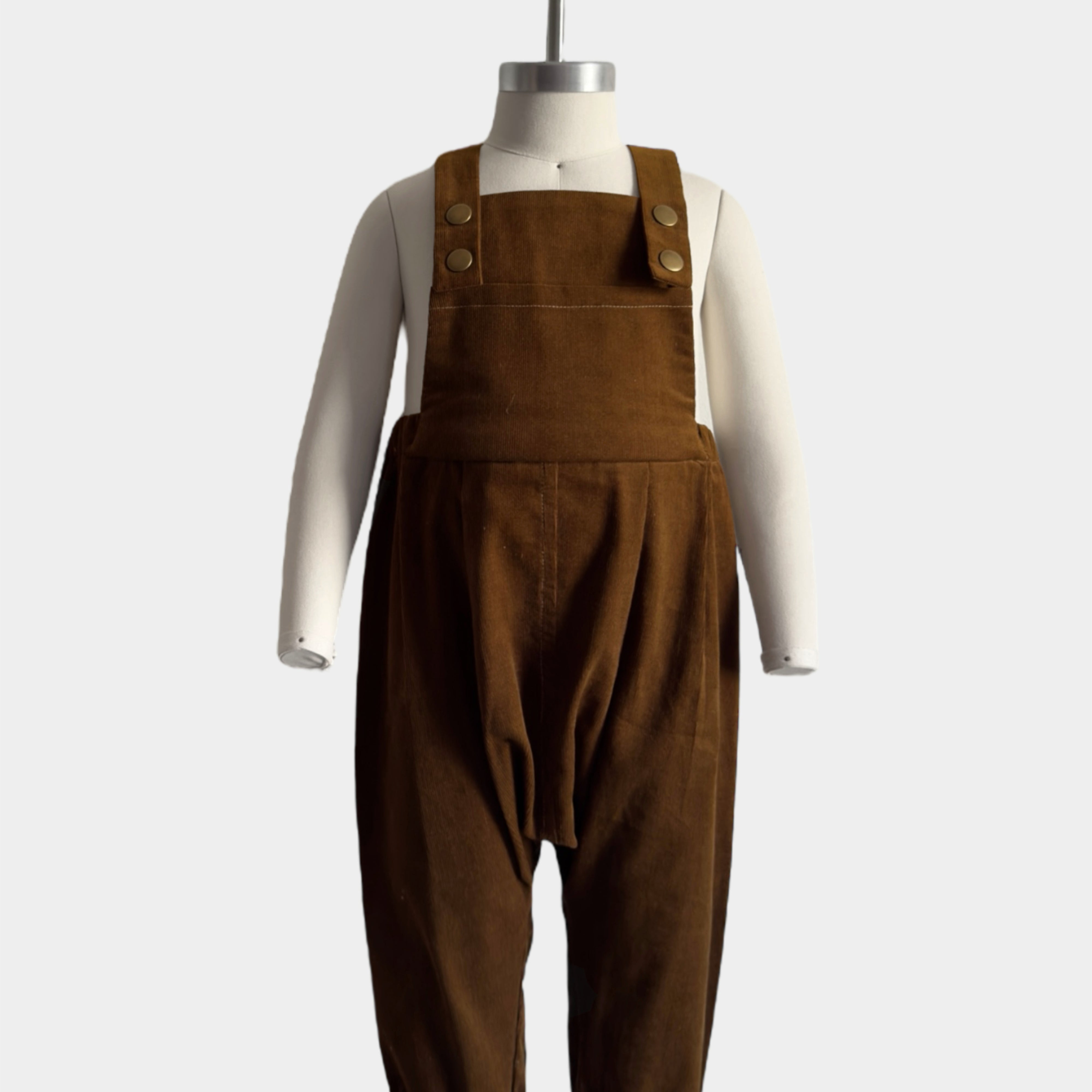 Front view of handmade cocoa brown long overalls displayed on a mannequin, highlighting intricate details such as the spacious bib pocket and stylish pleats, showcasing the craftsmanship of the handmade design.