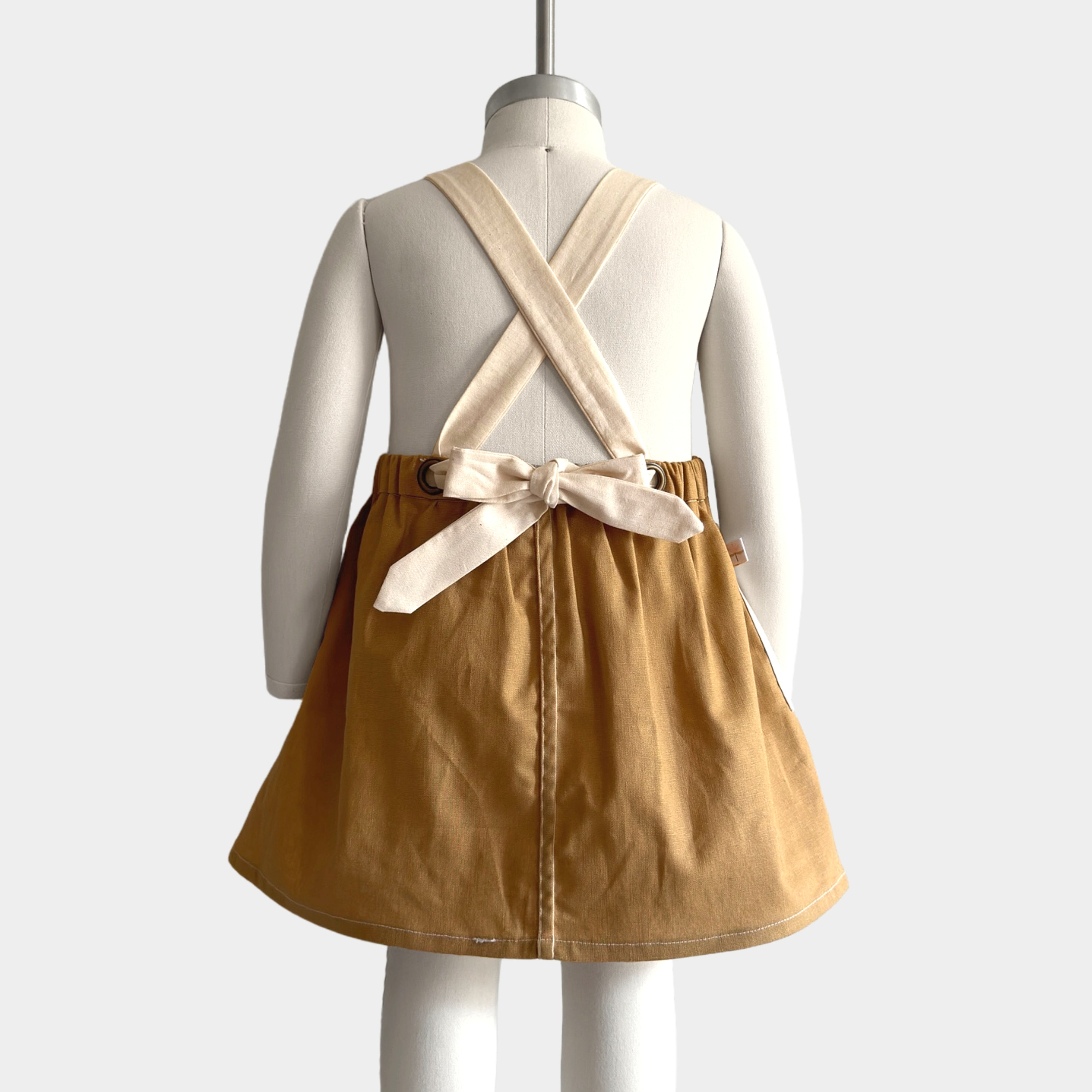 Back view of the Pinafore on a mannequin: The back of the Pinafore - Honey on a mannequin, emphasizing the generous strap design.