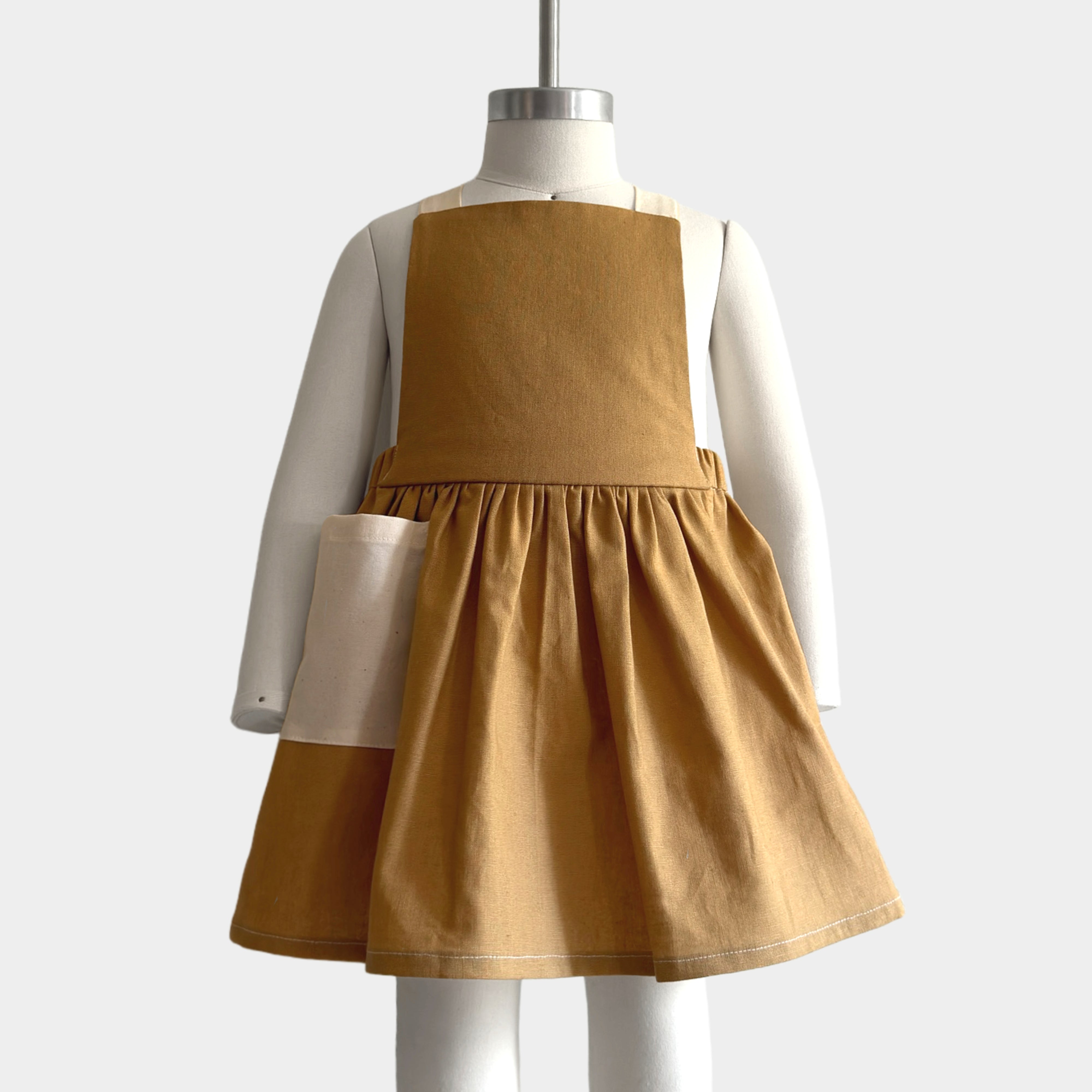 Front view of the Pinafore on a mannequin: The Pinafore - Honey displayed on a mannequin, highlighting its elegant silhouette and contrasting straps.