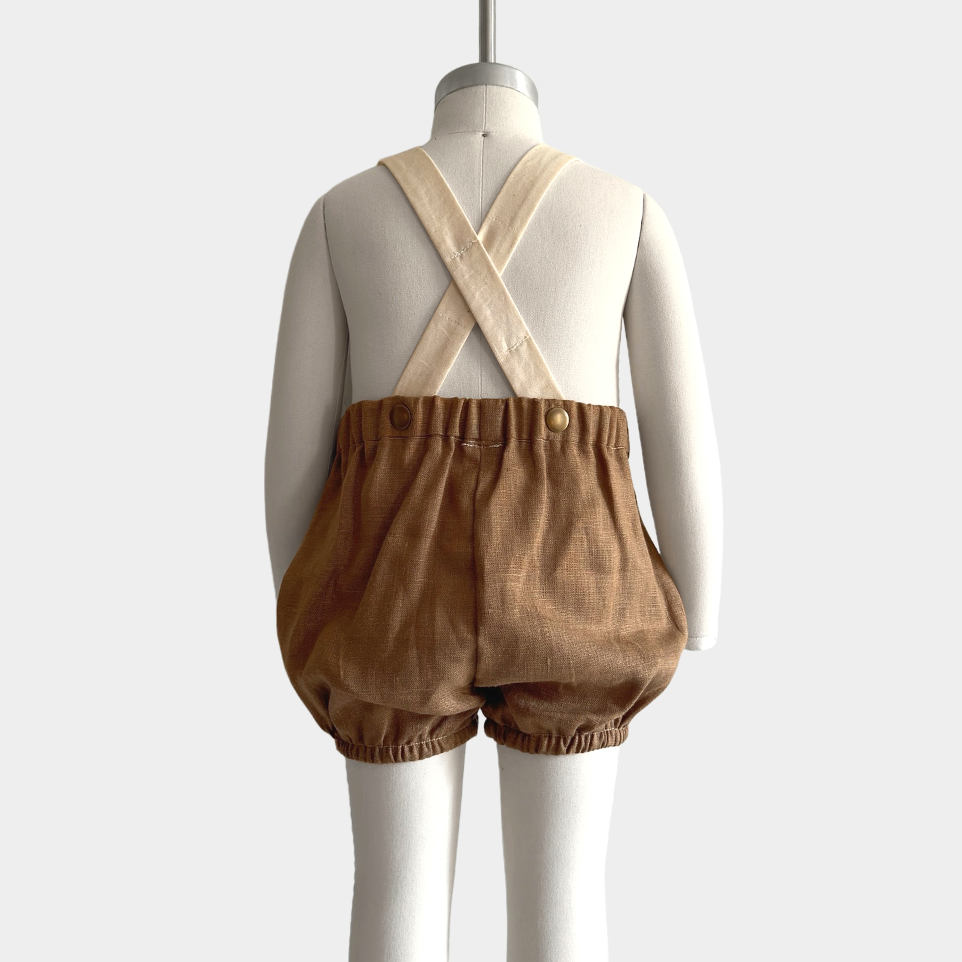 Back view on a mannequin of a andmade linen bubble romper in Beachwood, featuring adjustable contrasting straps in cream for a customizable fit and elasticized legs for easy movement during summer play. A gender-neutral design that combines timeless style with comfort, perfect for any occasion.