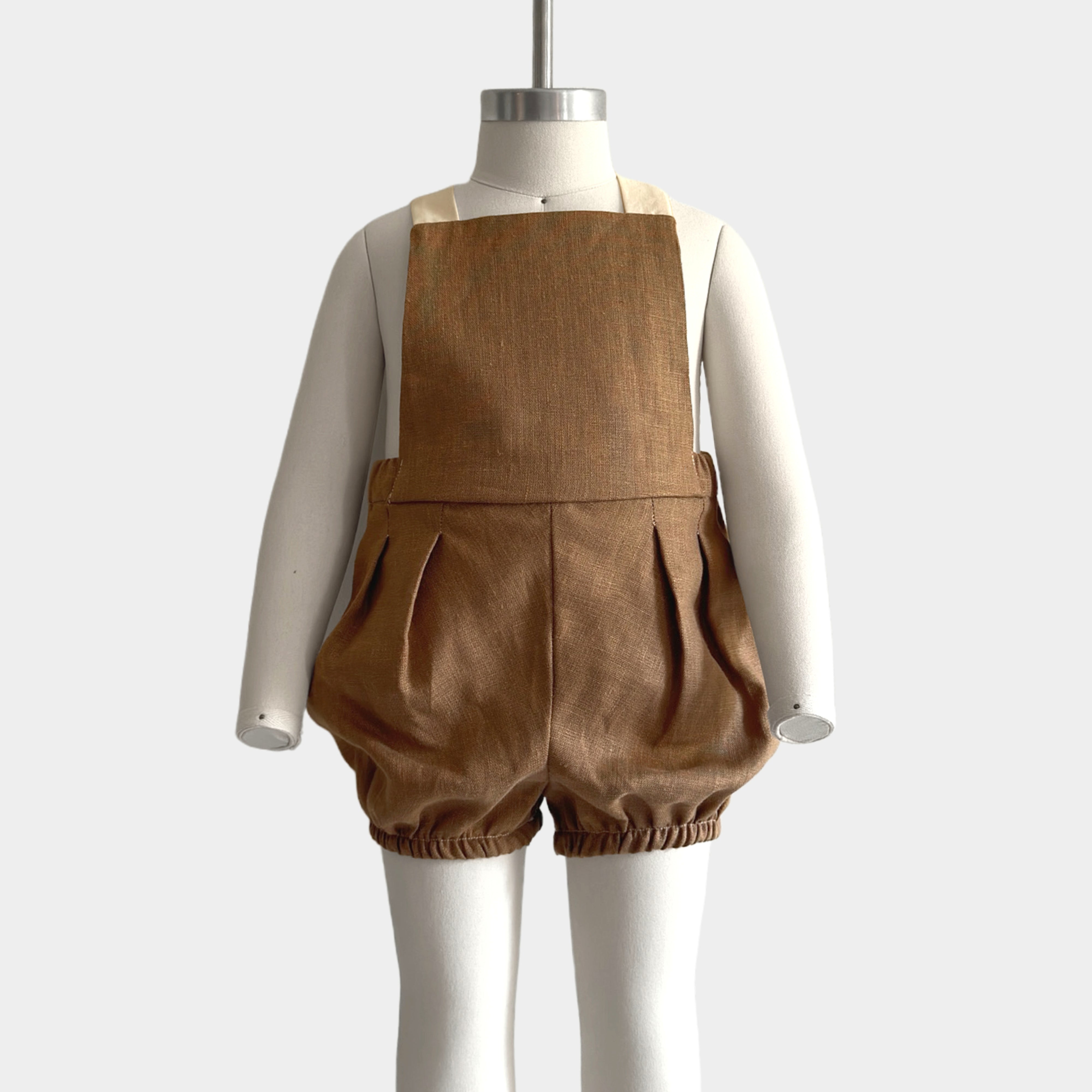 Front view on a mannequin of a handmade linen bubble romper in Beachwood, featuring adjustable contrasting straps in cream for a customizable fit and elasticized legs for easy movement during summer play. A gender-neutral design that combines timeless style with comfort, perfect for any occasion.