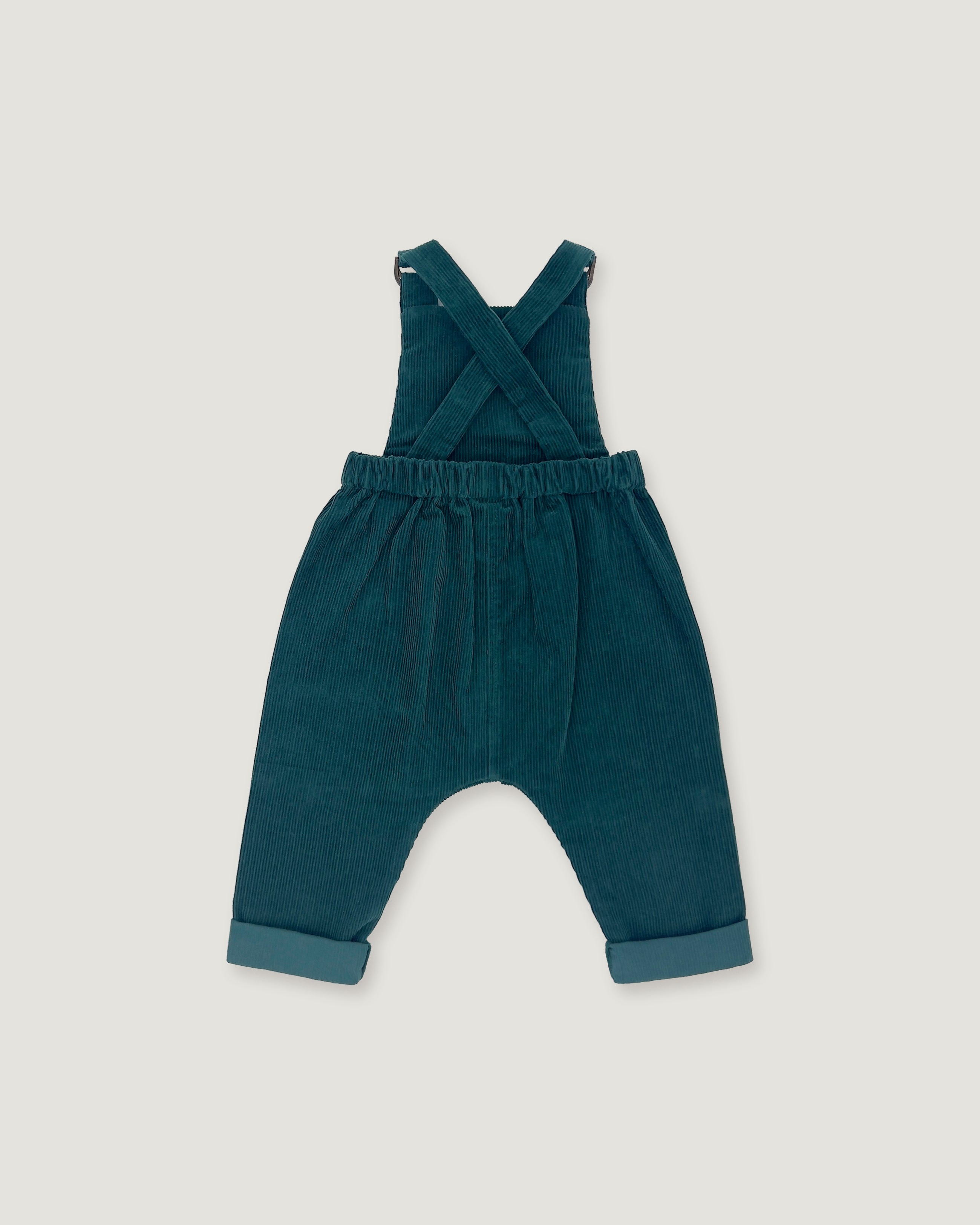 A pair of toddler corduroy overall jumpsuit in a deep teal blue-green color, featuring adjustable shoulder straps that cross over the chest and cuffed harem-style legs, shown flat on a light gray background.