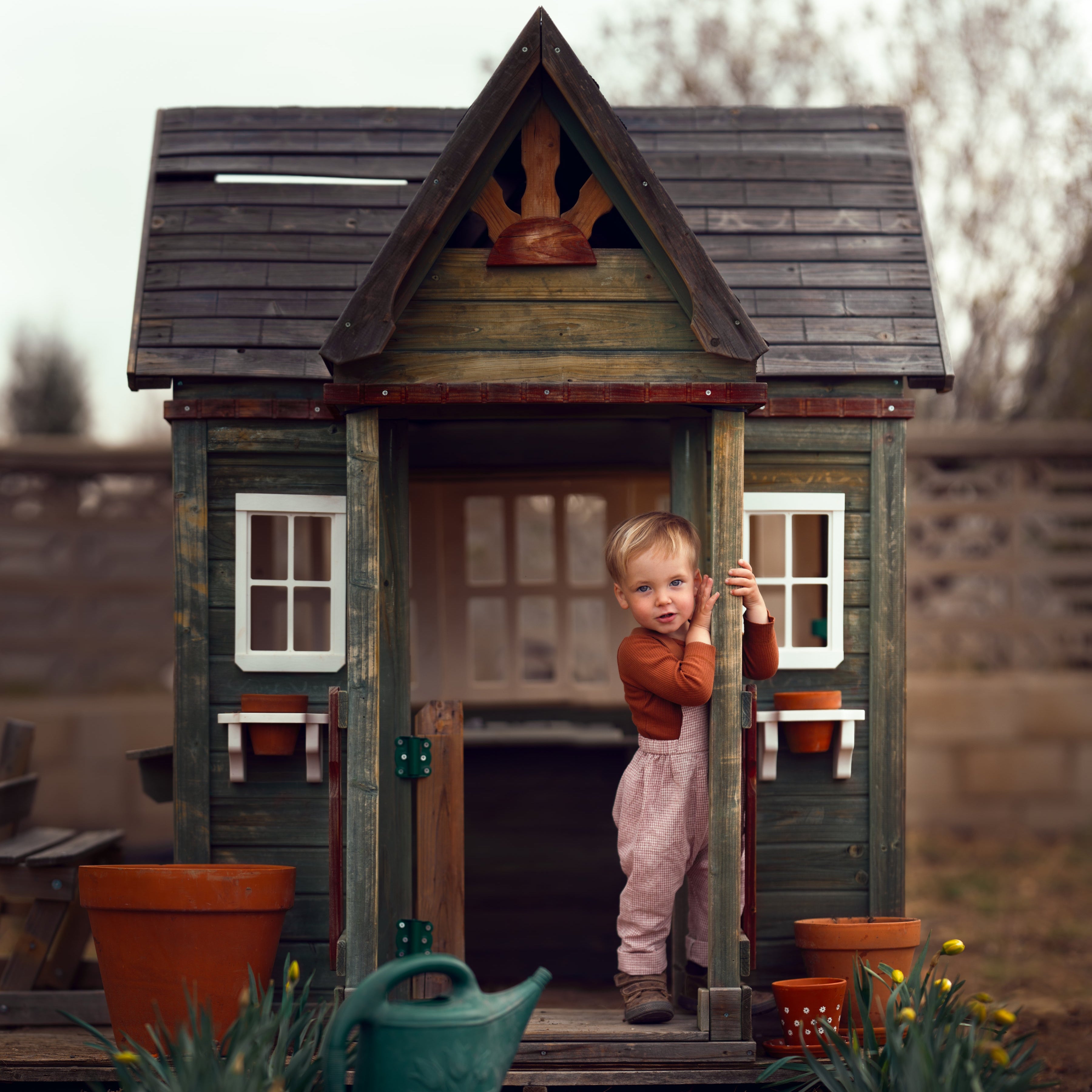 little boy in checkered overalls standing in front of a toy barn