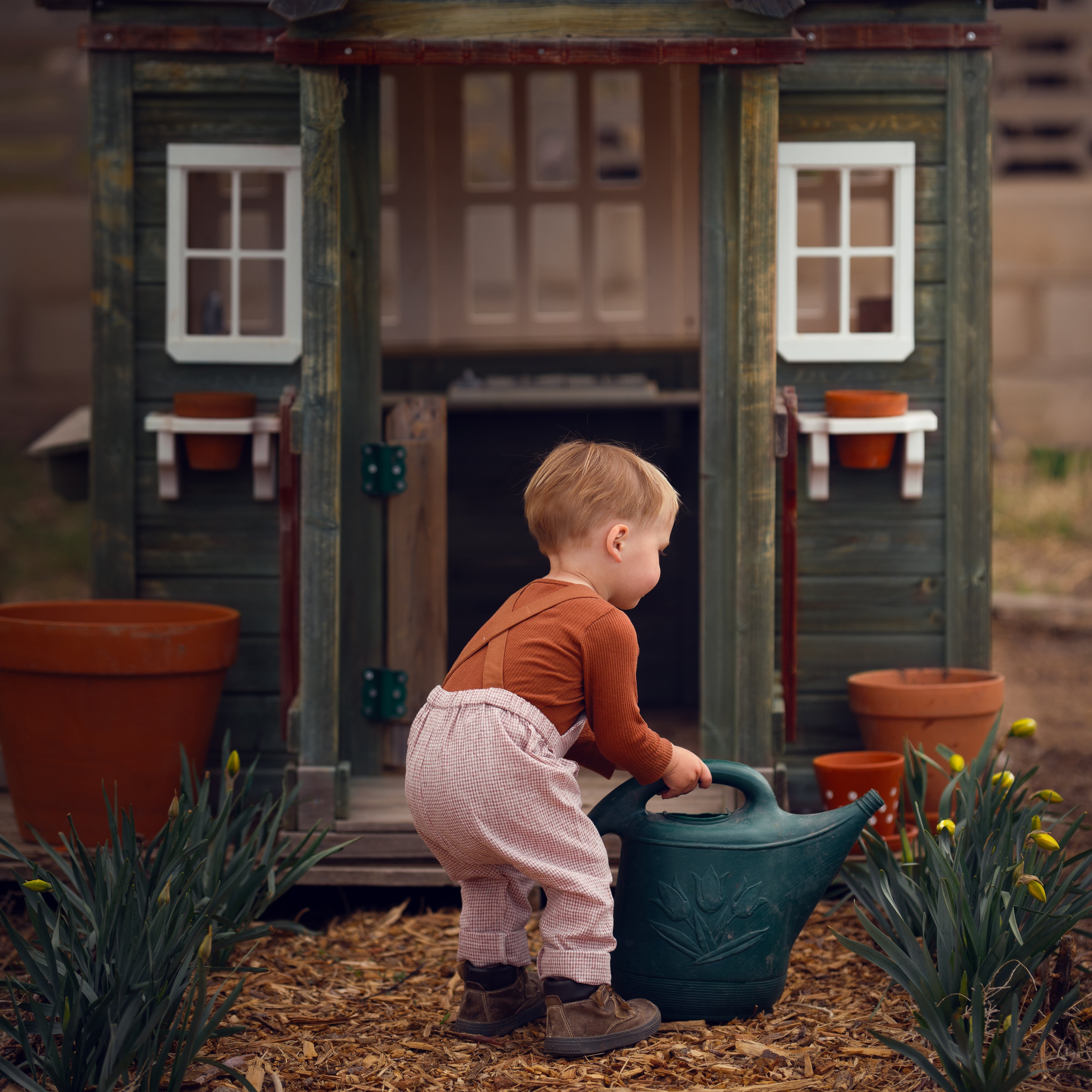 little boy in checkered overalls in front of a barn